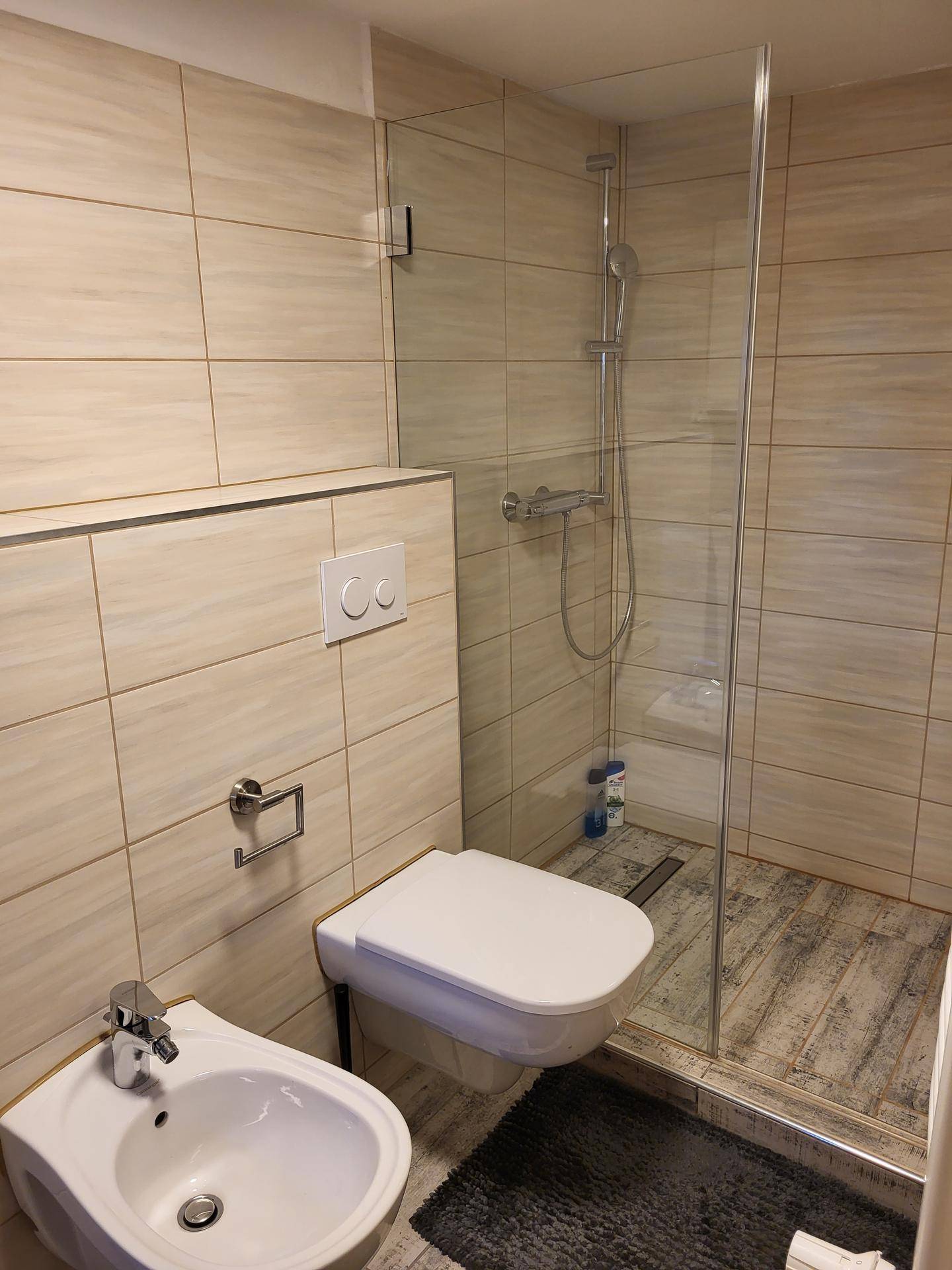 Modernes Badezimmer im Untergeschoss mit beigefarbenen Fliesen, Duschkabine und Bidet.