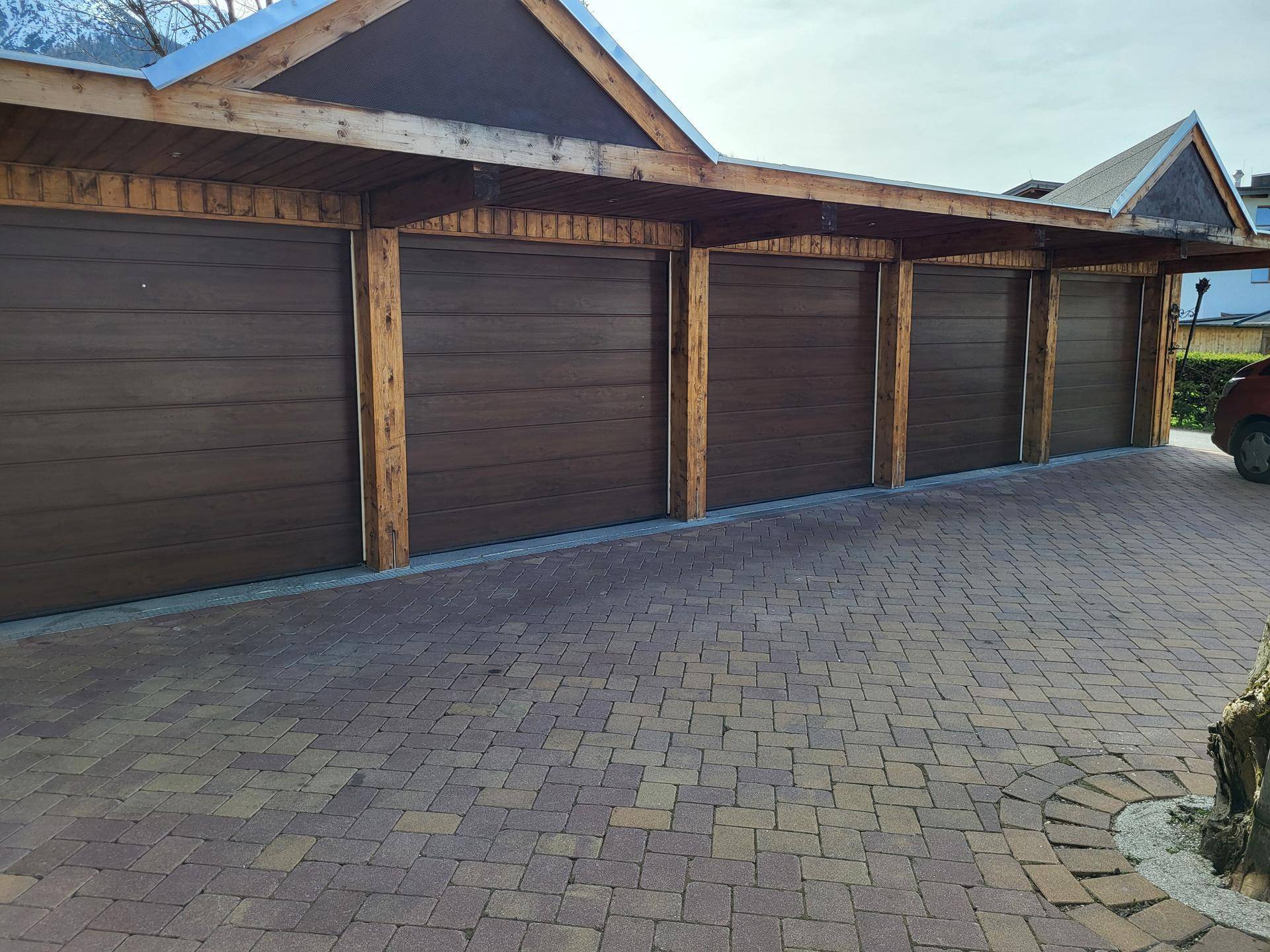Reihe von braunen Garagentoren mit Holzrahmen und gepflasterter Einfahrt.