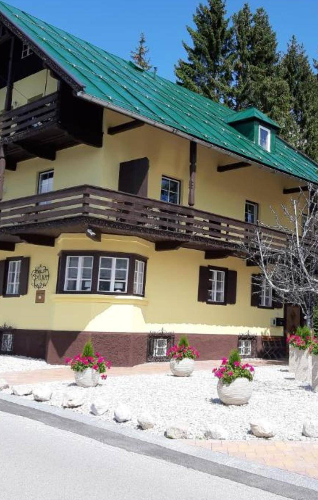 Traditionelles Gebäude im alpinen Stil mit gelber Fassade, Holzbalkonen und grünem Satteldach.