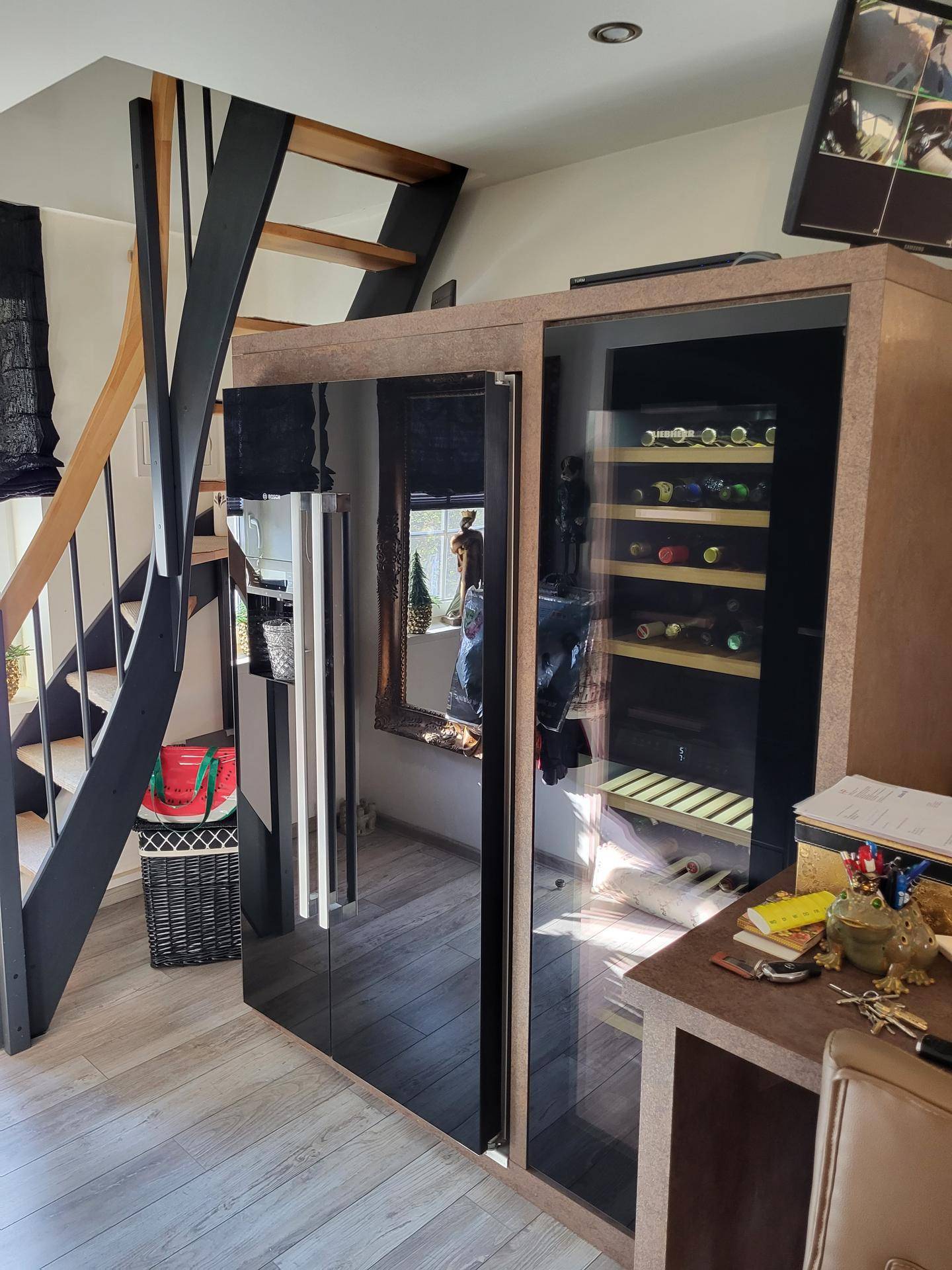 Moderner Wohnbereich mit Weinkühlschrank, Kühlschrank und offener Treppe.
