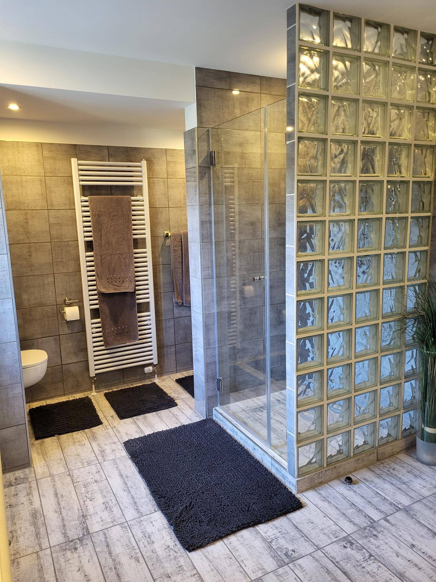 Modernes Badezimmer mit grauen Fliesen, Duschkabine aus Glas und beheiztem Handtuchhalter.
