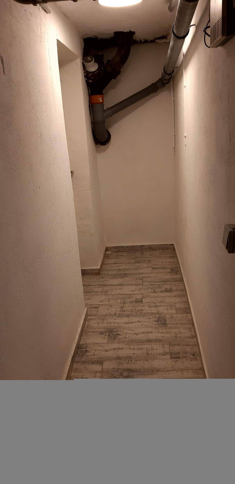 Schmaler Versorgungsraum mit sichtbaren Rohren und Fliesenboden.