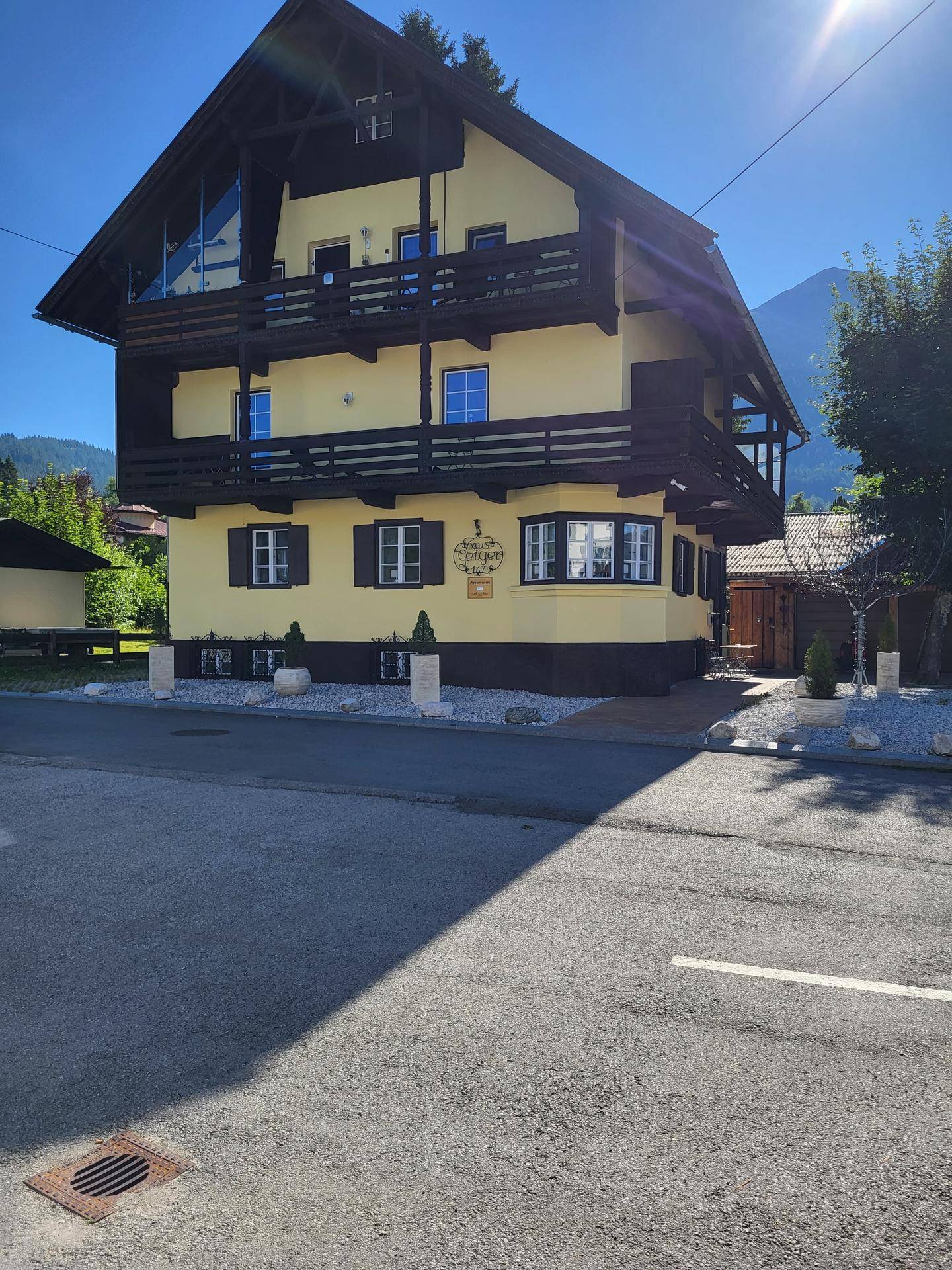 Sonnenbeschienenes gelbes Haus mit Holzbalkonen und grünem Dach in alpiner Umgebung.