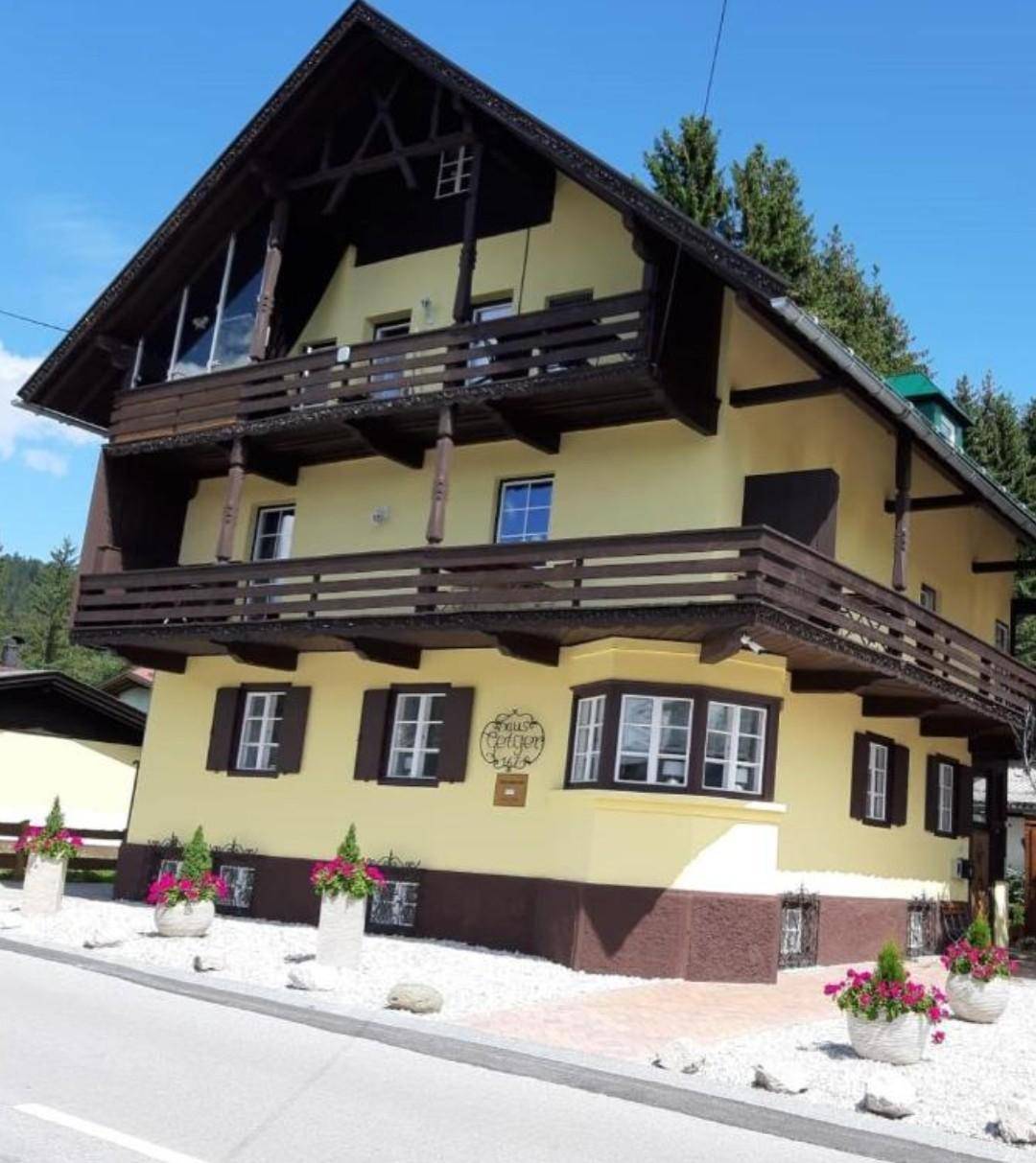 Charmantes Gebäude im alpinen Stil mit gelber Fassade, braunen Akzenten und mehreren Balkonen.