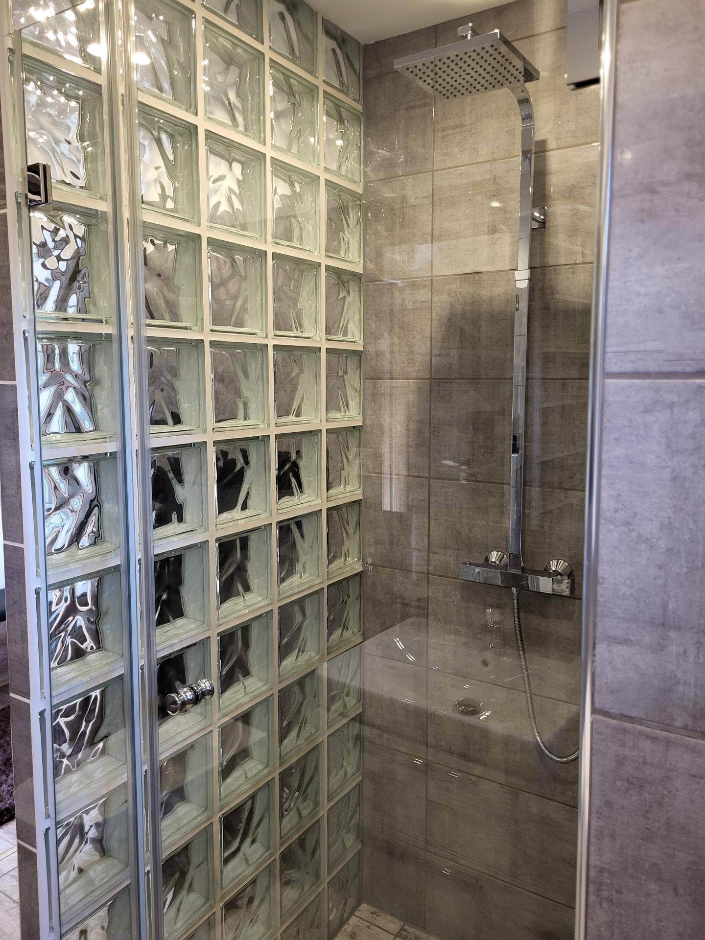 Duschbereich mit Glasbausteinwand und Regendusche in einem modern gefliesten Badezimmer.