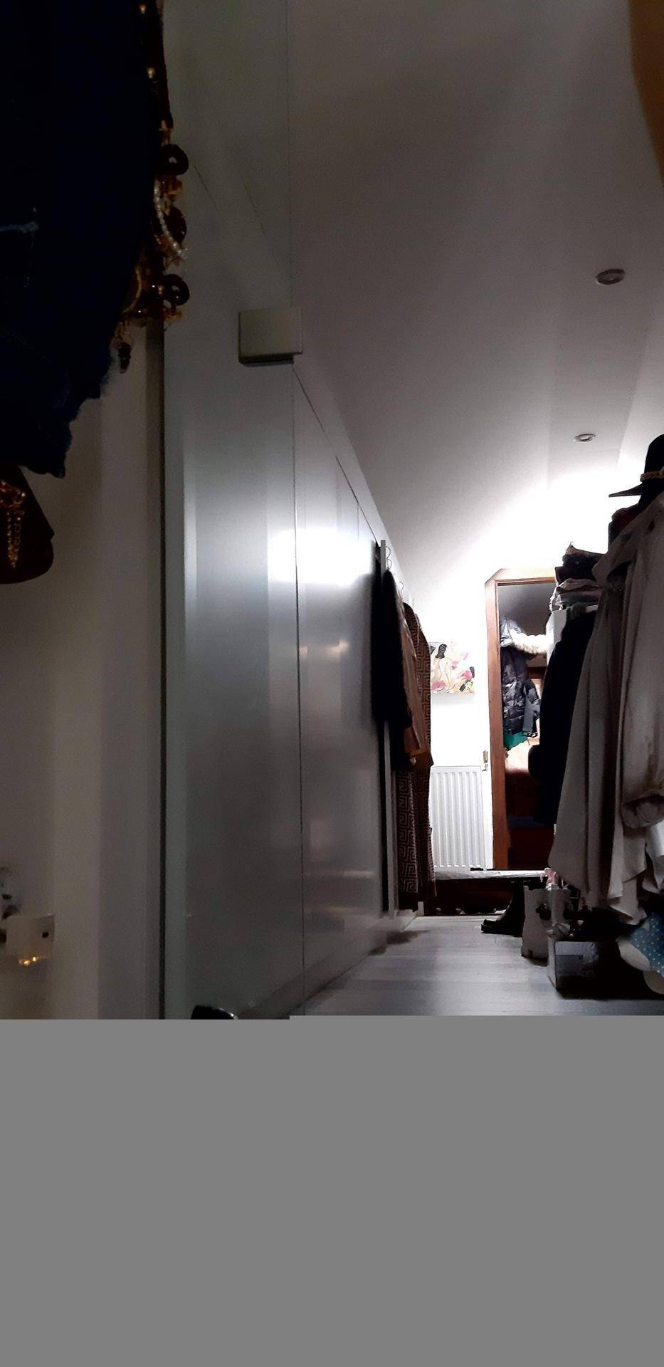 Dunkler Flur mit Kleidern an den Wänden und begrenzter Sichtbarkeit.