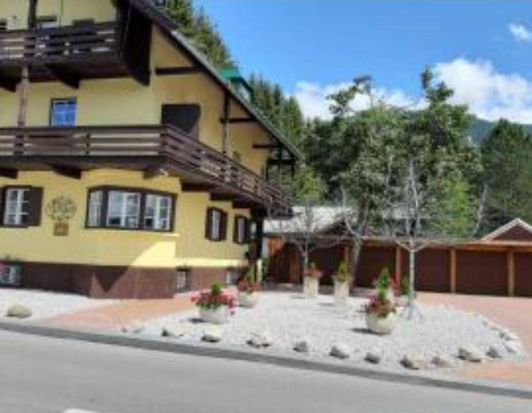 Gebäude im alpinen Stil mit gelb-brauner Fassade, Balkonen und gepflegtem Vorgartenbereich.