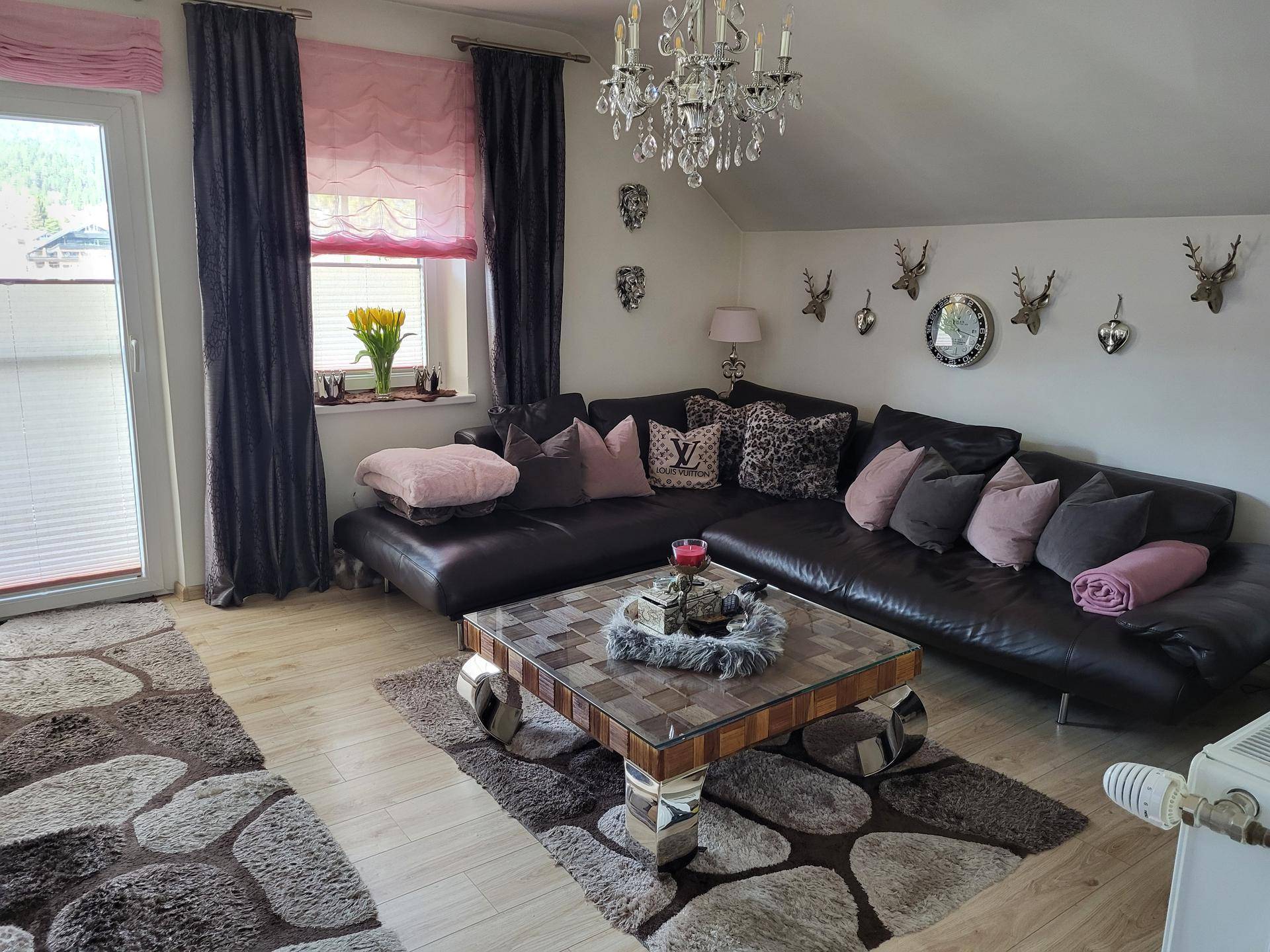 Geräumiges Wohnzimmer mit großer Eckcouch, Kronleuchter und Zugang zum Balkon.