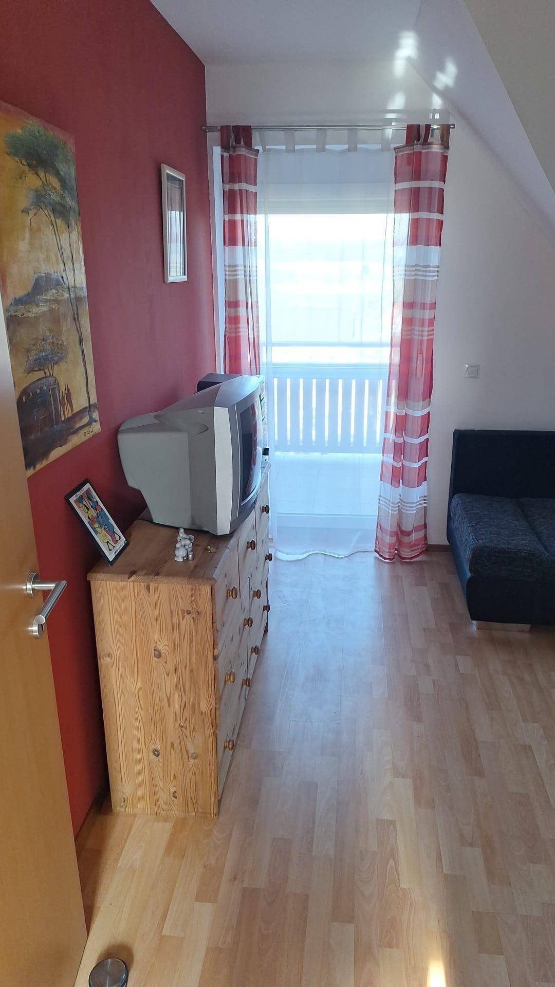 Wohnbereich mit Laminatboden, Kommode und Zugang zu einem kleinen Balkon.