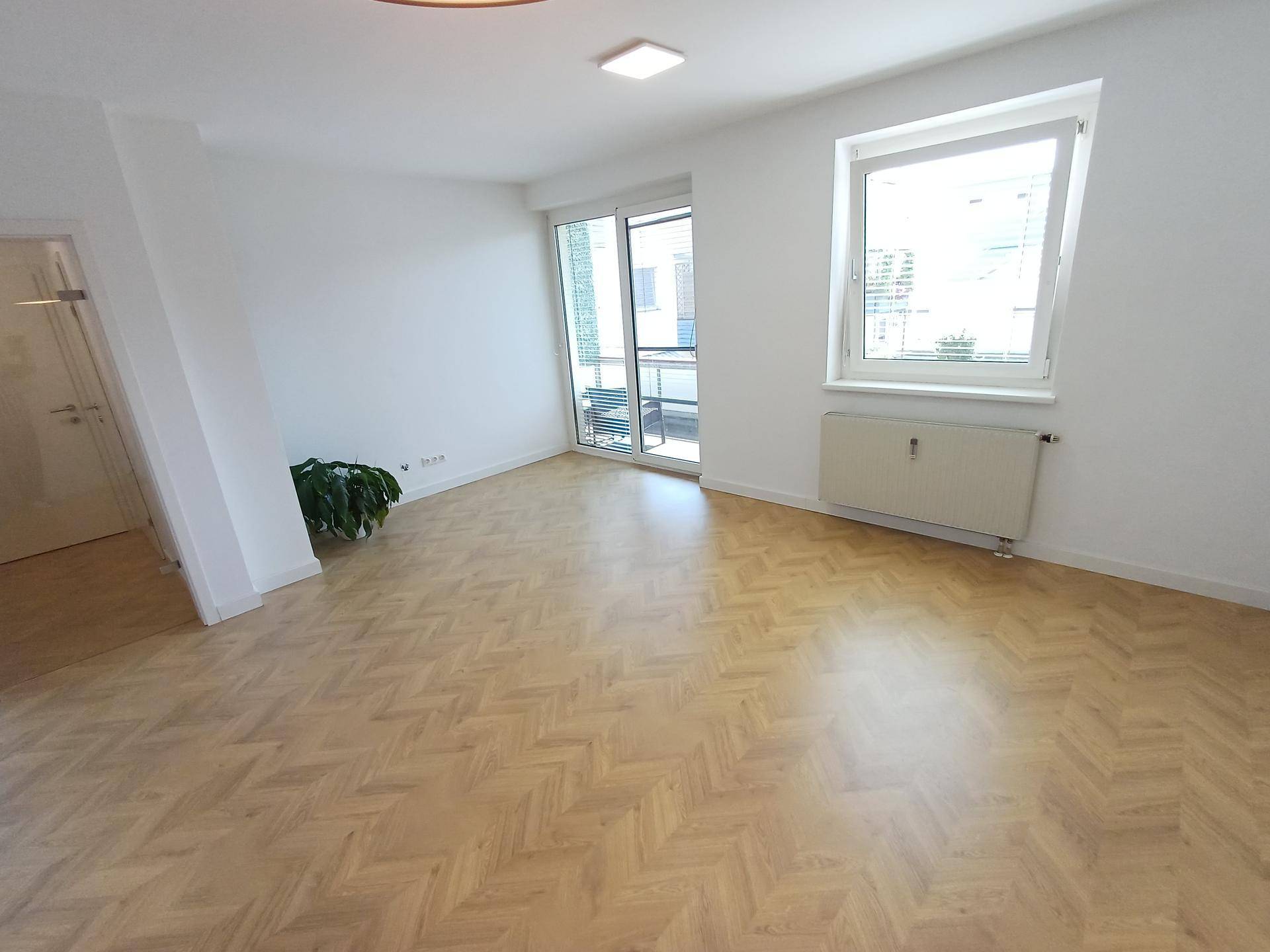 Helles, leeres Wohnzimmer mit Fischgrätparkett und Zugang zum Balkon, bereit zur individuellen Gestaltung.