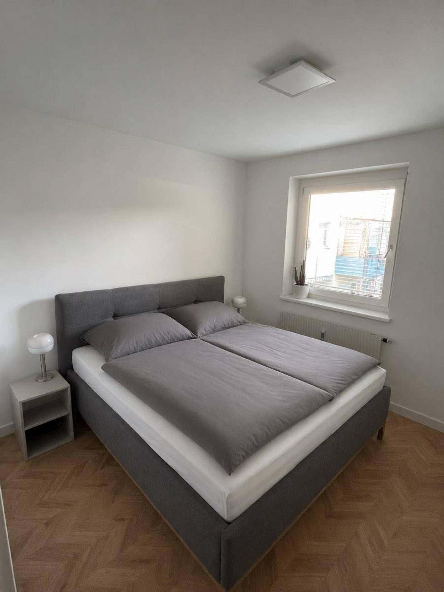 Helles Schlafzimmer mit Doppelbett und Nachttischen, ausgestattet mit Parkettboden und Fenster.