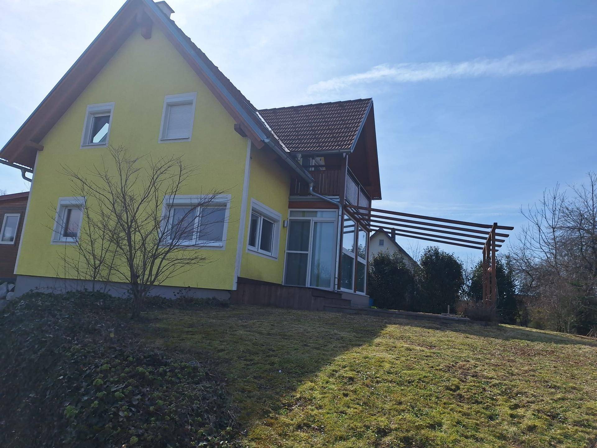 Ansicht des gelben Hauses mit großem Rasenbereich und einem Wintergarten an der Seite.