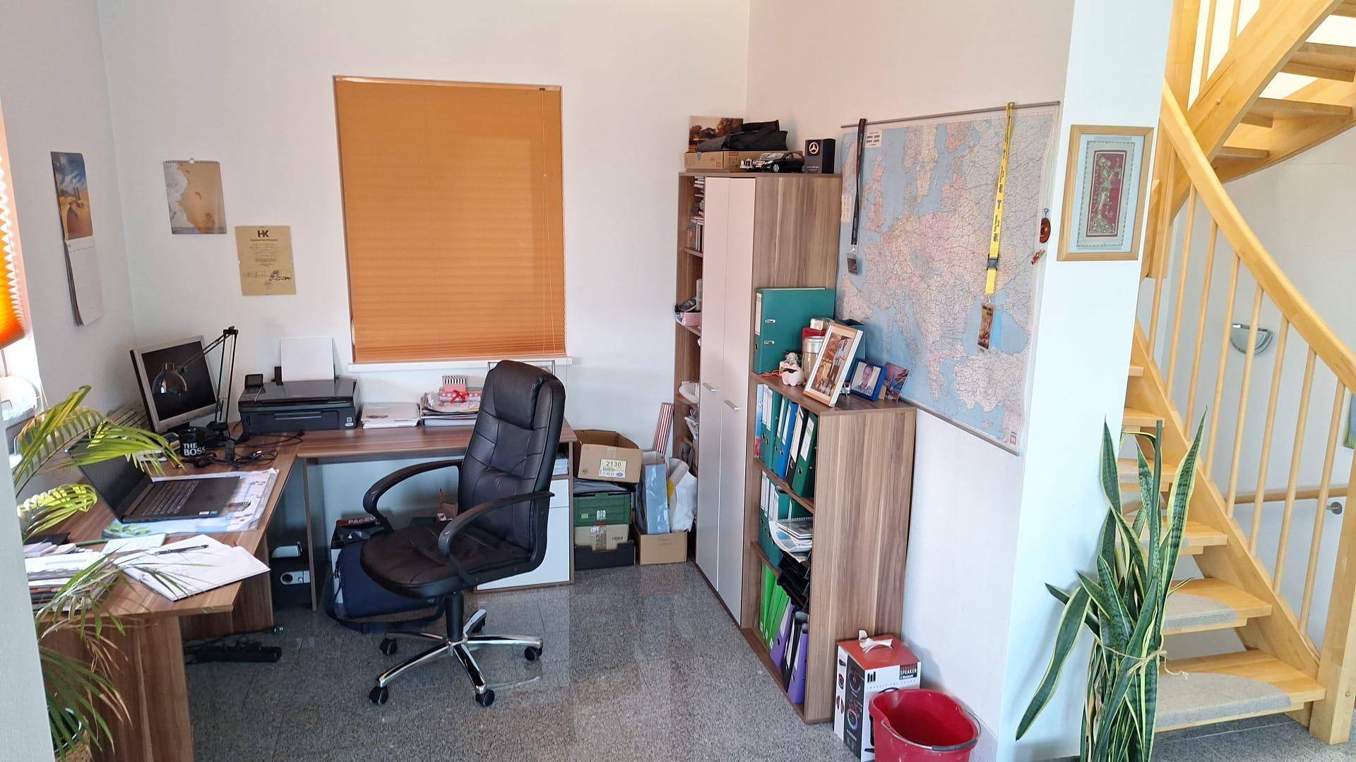 Helles Arbeitszimmer mit Schreibtisch, Bürostuhl und Holztreppe zum Obergeschoss.