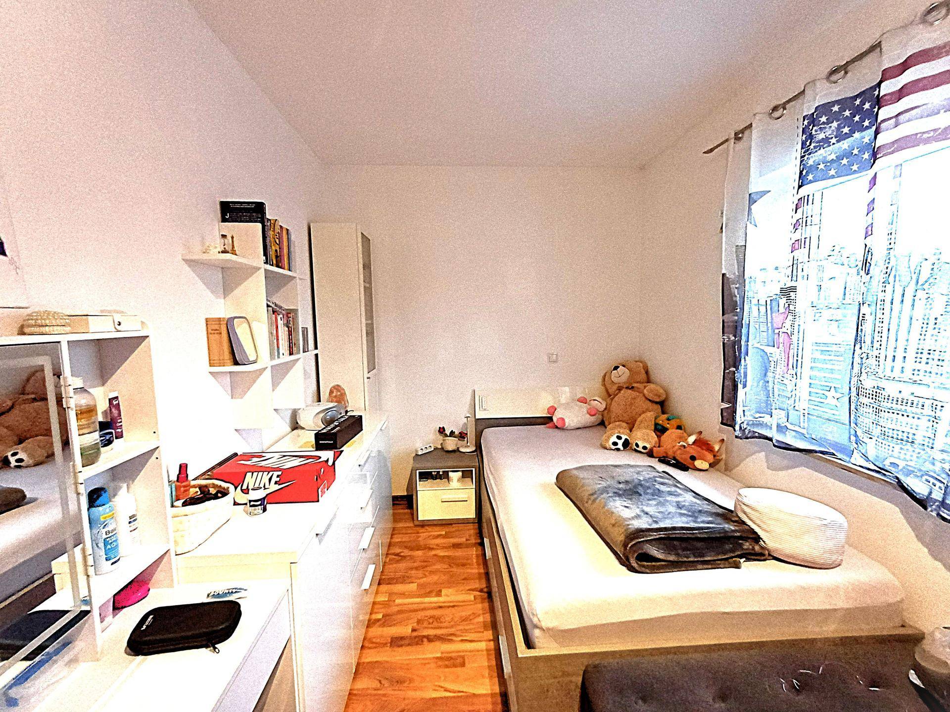 Kinderzimmer mit Einzelbett, Regalen und Spielzeug, hell und freundlich gestaltet.