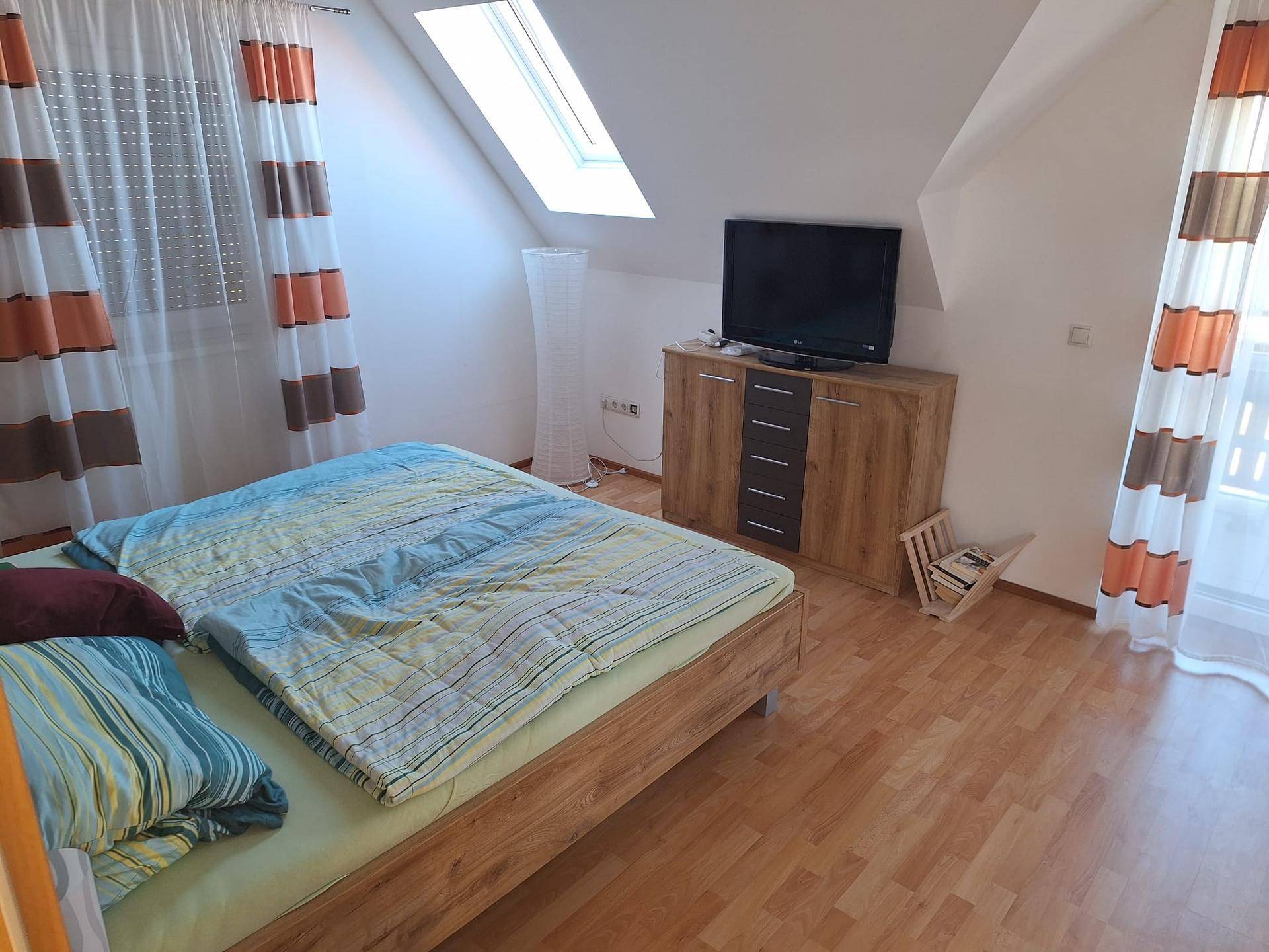 Gemütliches Schlafzimmer mit Laminatboden, Doppelbett und Zugang zum Balkon.