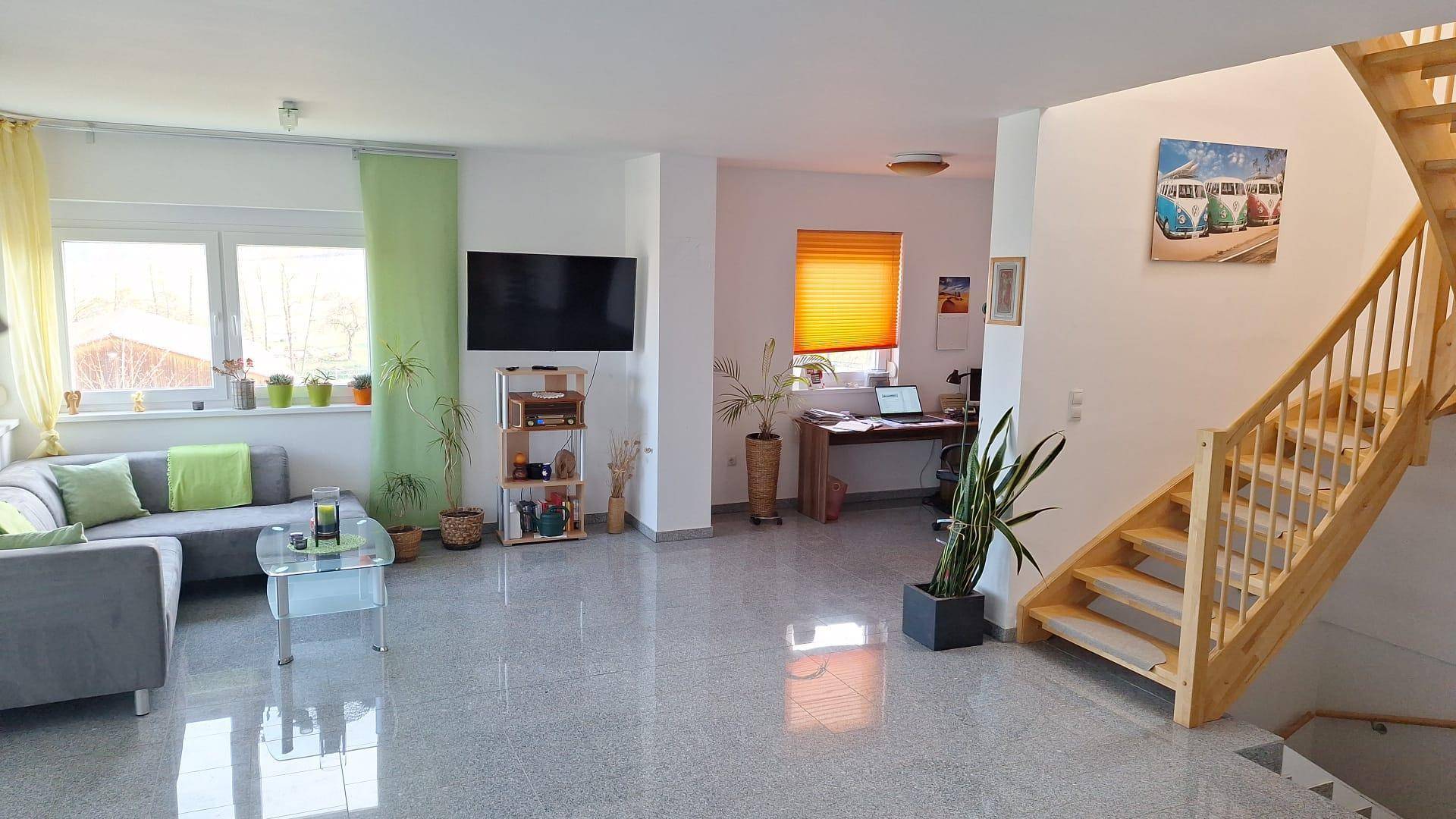 Offener Wohn- und Essbereich mit Granitboden, Sofa und Holztreppe.