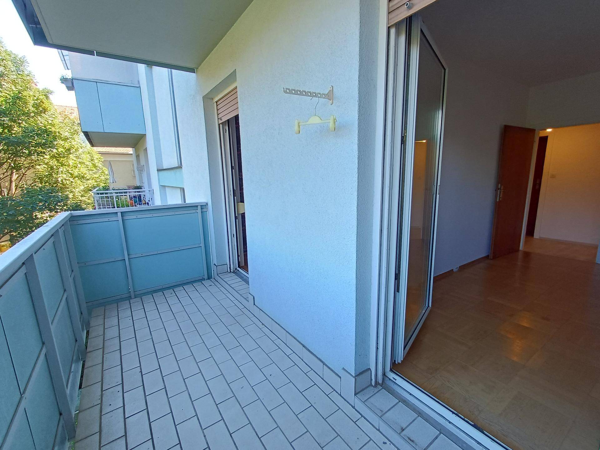 Überdachter Balkon mit hellen Fliesen und Blick auf die umliegenden Gebäude und Bäume.
