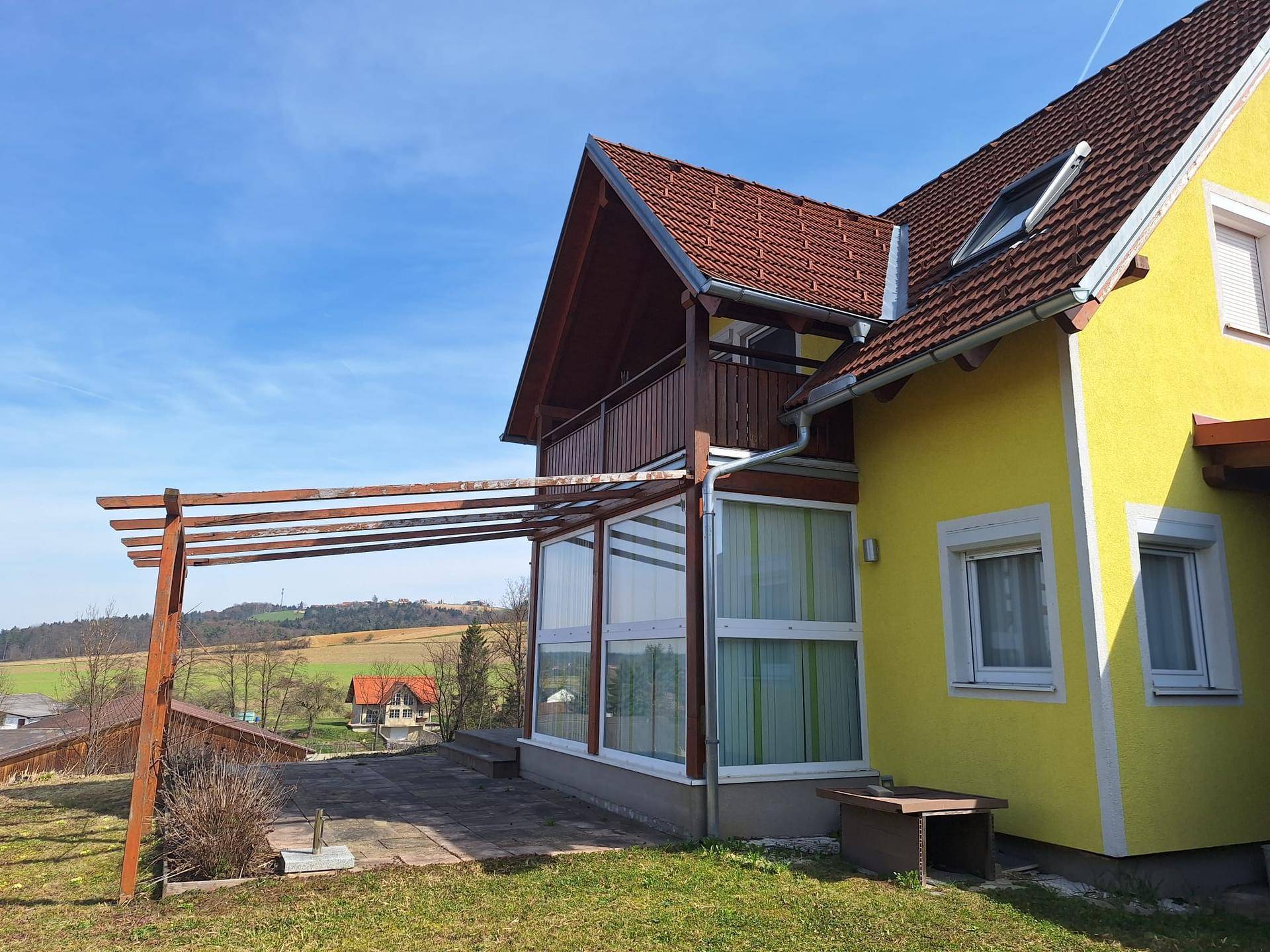 Seitenansicht des Hauses mit Wintergarten, Pergola und weitem Blick über die Landschaft.