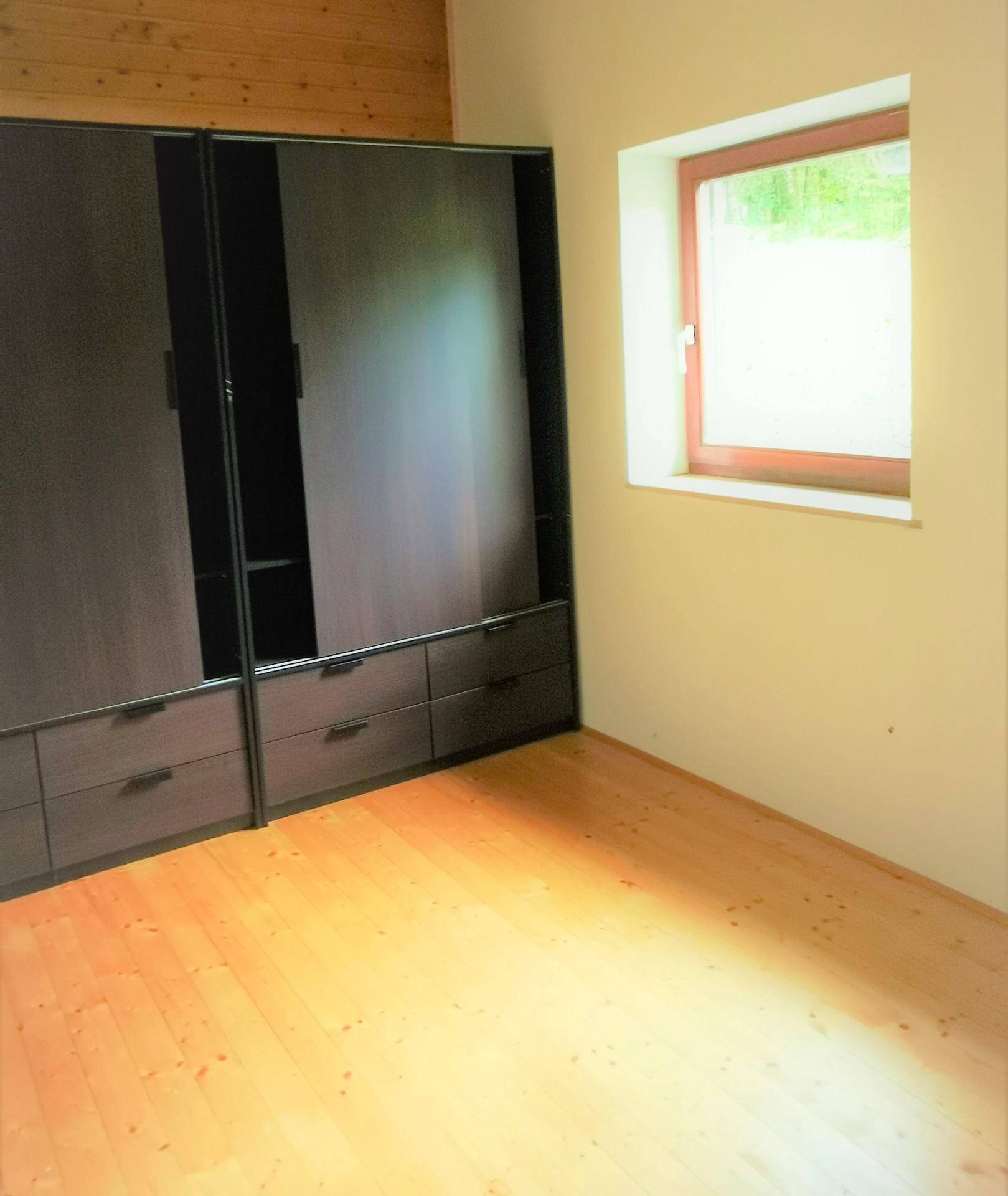 Schlafzimmer mit hellem Holzboden und einem großen, dunklen Einbauschrank.