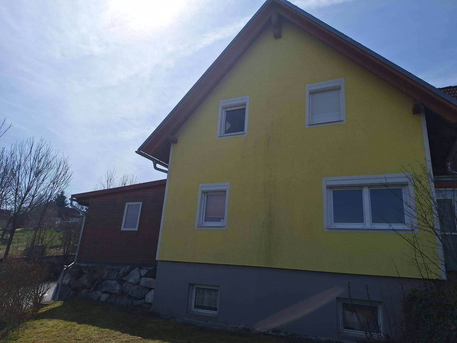Rückansicht des gelben Hauses mit Fenstern und einem kleinen Anbau aus Holz.