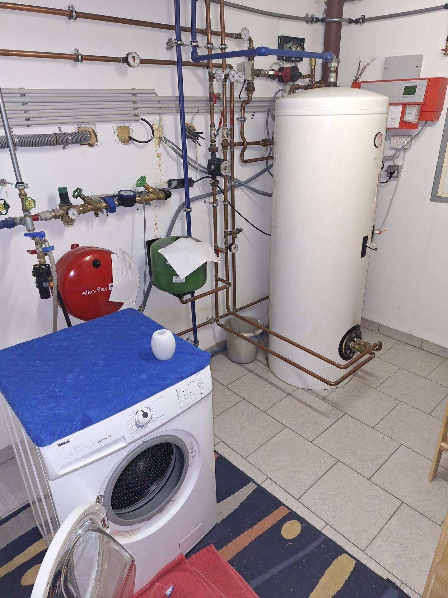 Hauswirtschaftsraum mit Waschmaschine, Warmwasserspeicher und sichtbaren Installationen.