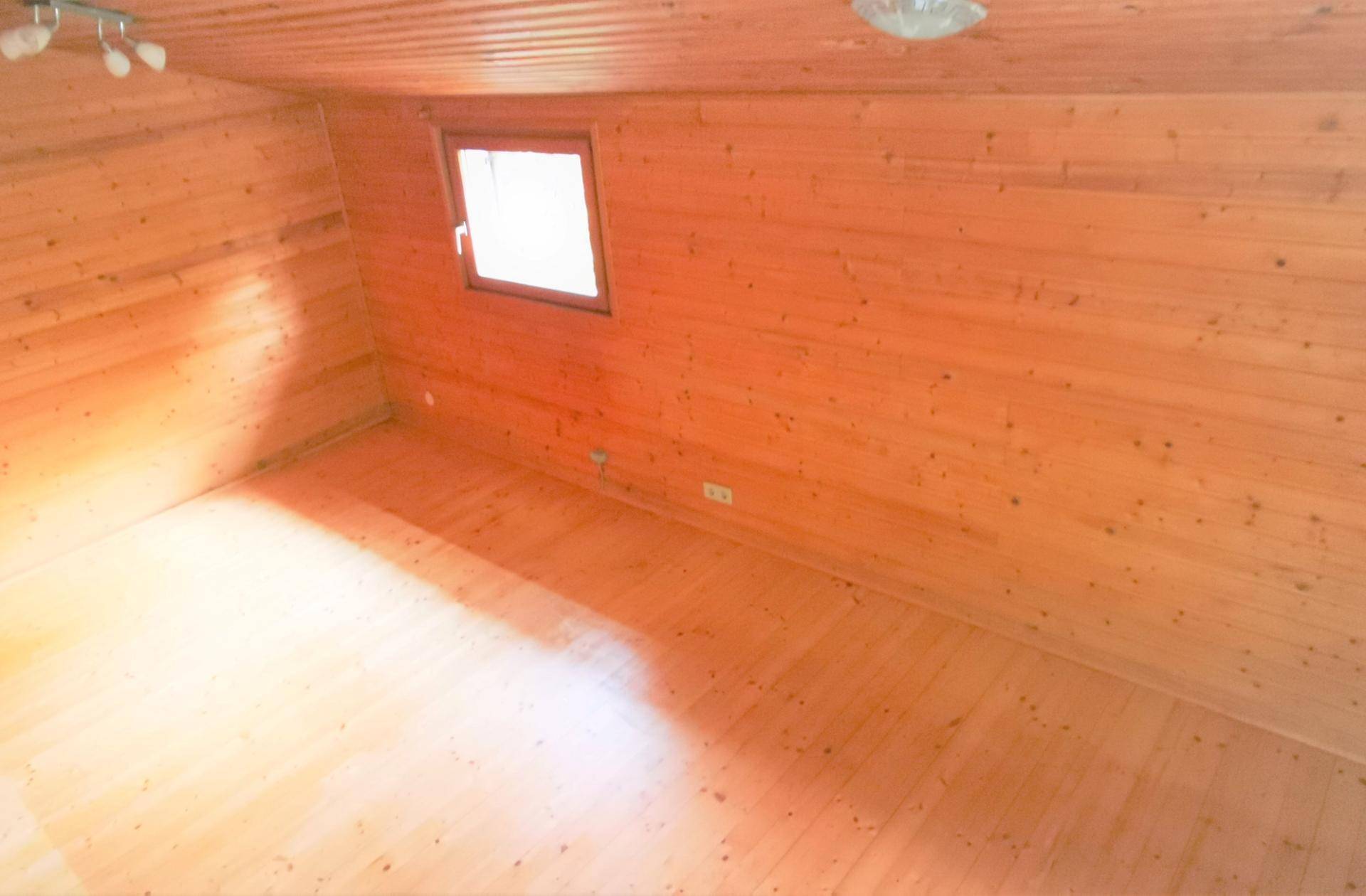 Schlafzimmer mit warmen Holzwänden und Holzboden, durch ein Fenster gut belichtet.