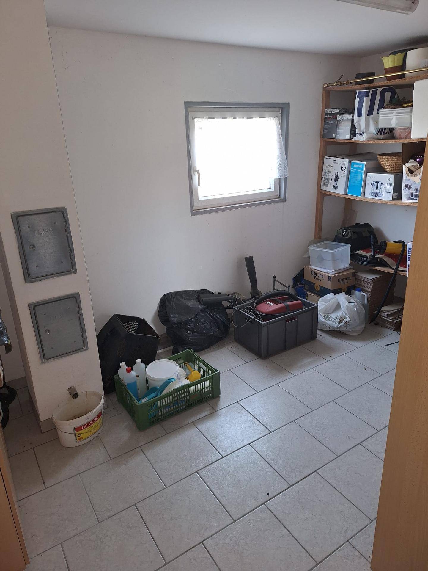 Abstellraum mit Fliesenboden, einem Fenster und verschiedenen Lagergegenständen.