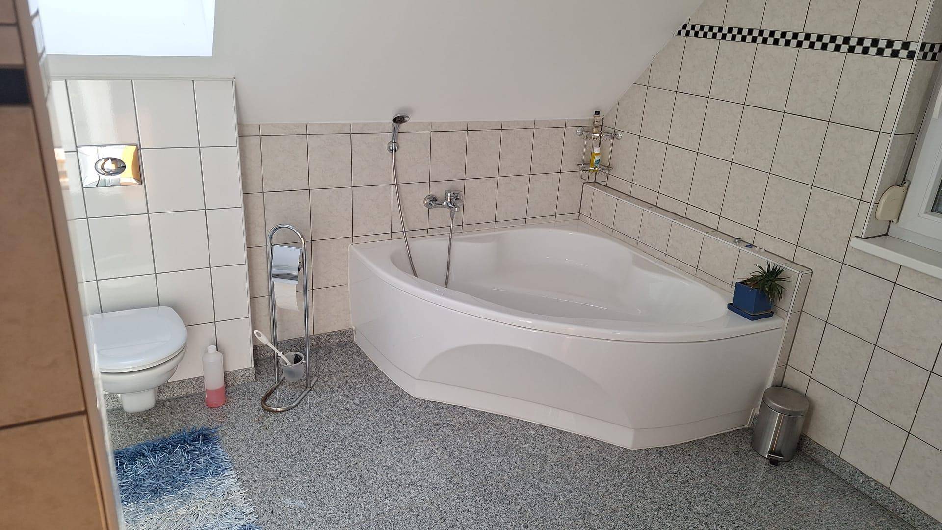 Geräumiges Badezimmer mit Eckbadewanne, WC und Fliesen an Wänden und Boden.