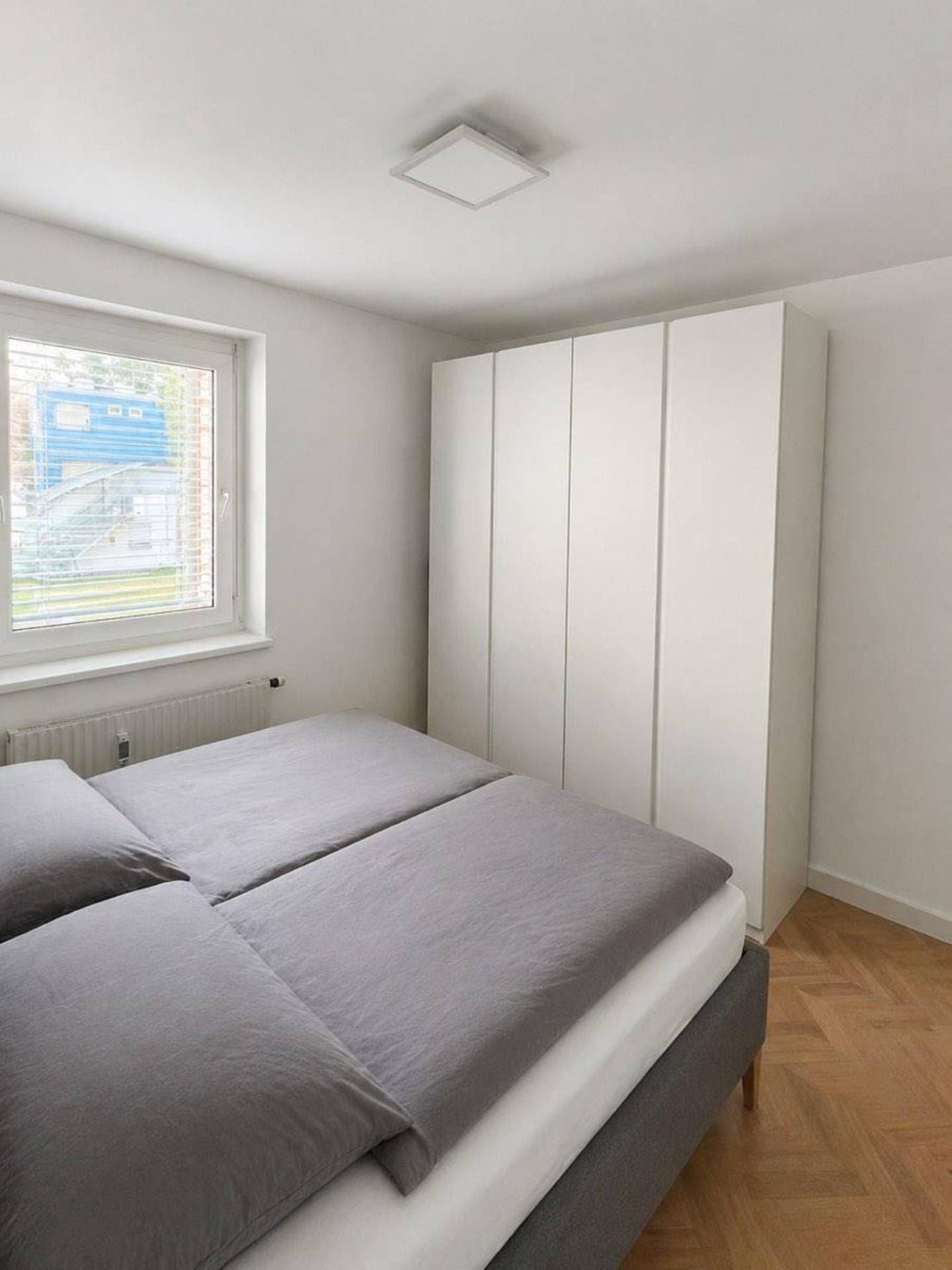 Schlafzimmer mit Doppelbett, weißem Kleiderschrank und Parkettboden, hell und funktional eingerichtet.