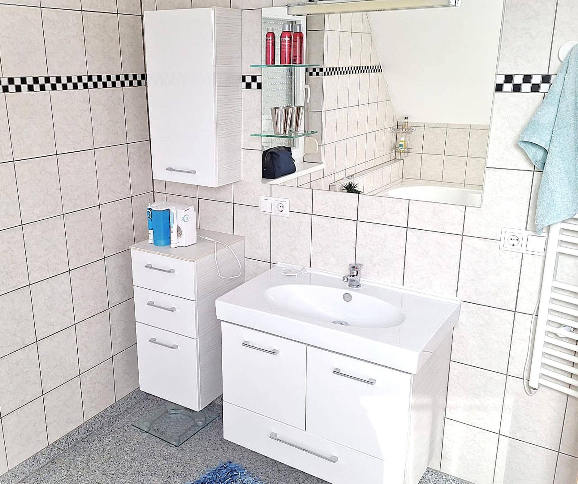 Helles Badezimmer mit weißen Fliesen, modernem Waschtisch und Spiegelschrank.