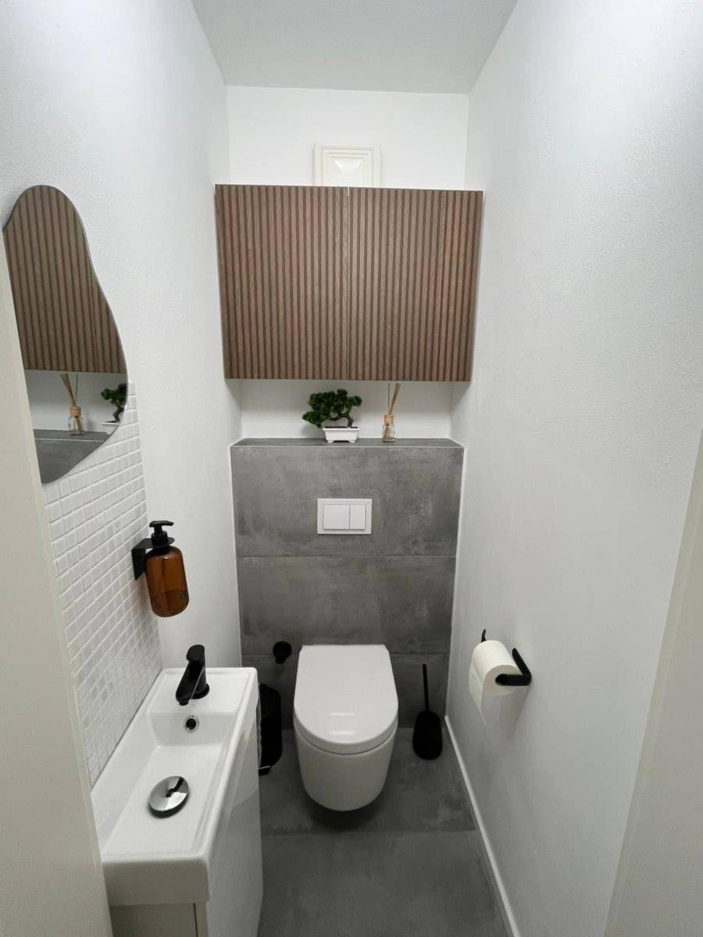 Modernes Gäste-WC mit Wand-WC, kleinem Waschbecken und stilvoller Holzverkleidung.