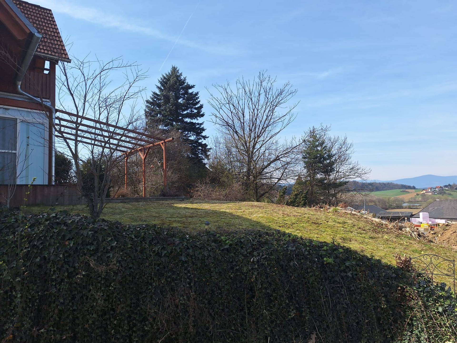 Gartenbereich mit einer Holzpergola und Blick auf die umliegende Natur und Hügel.
