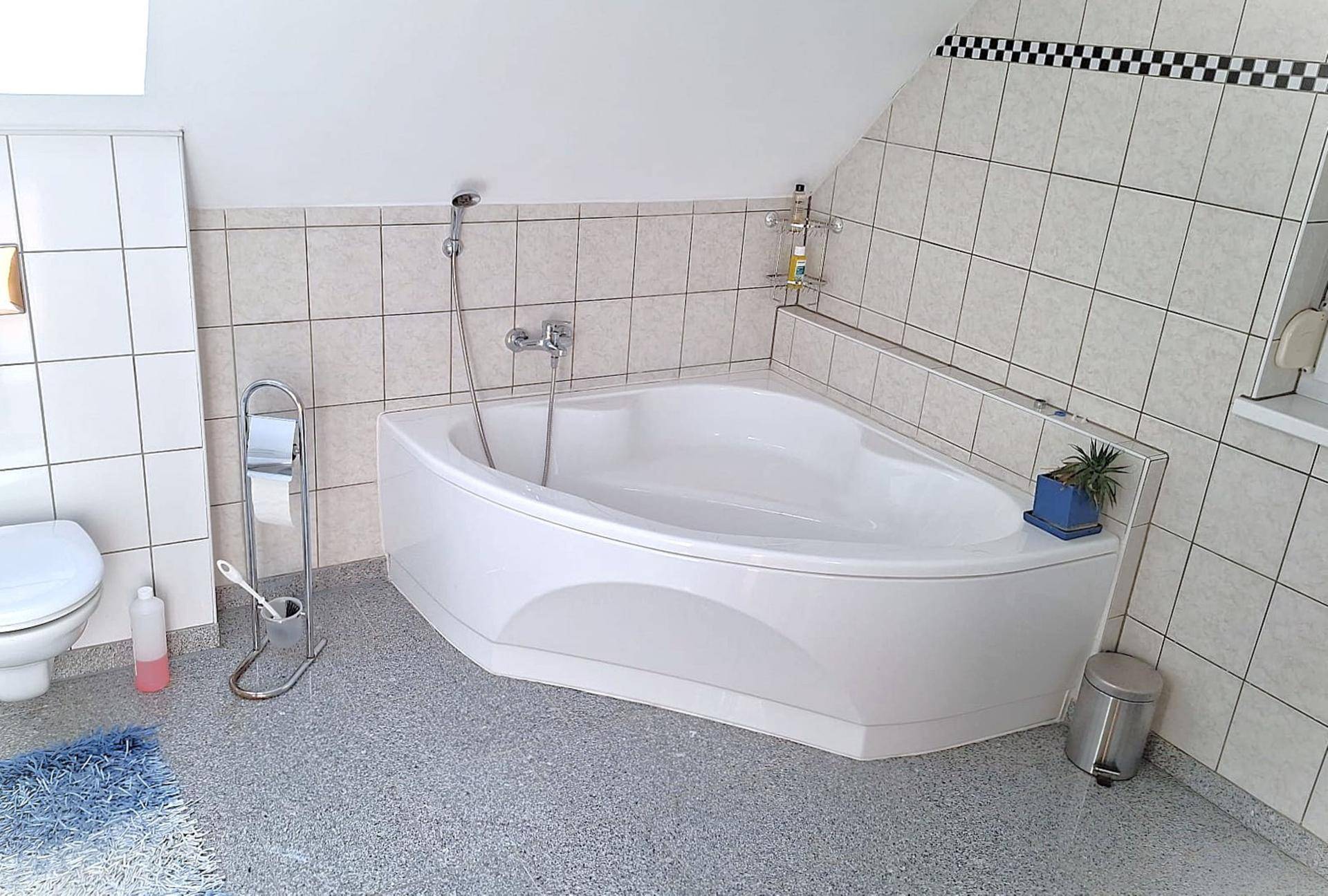 Badezimmer im Dachgeschoss mit Eckbadewanne, WC und hellen Fliesen.