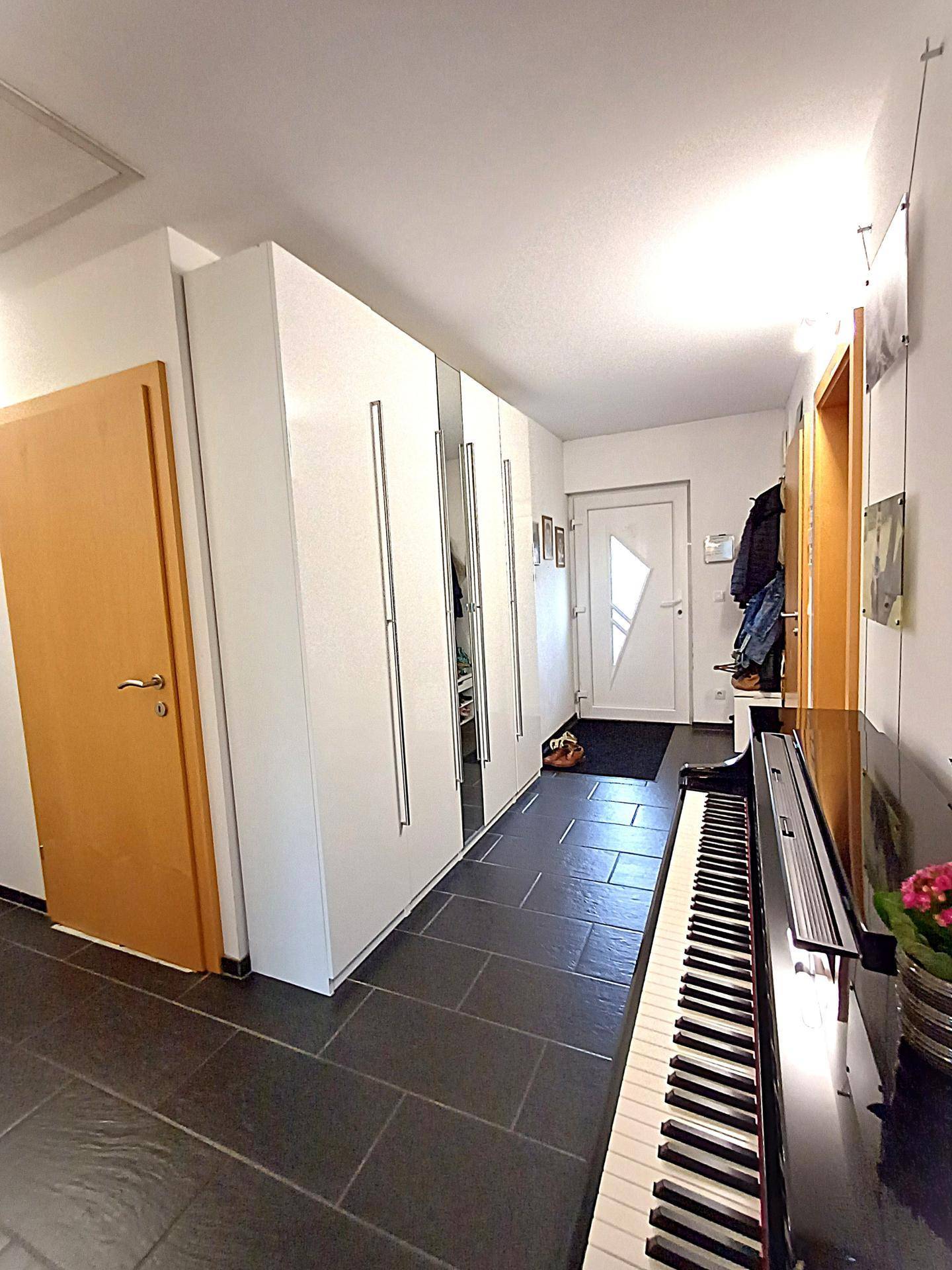 Heller Flur mit Einbauschränken, Klavier und dunklem Fliesenboden.