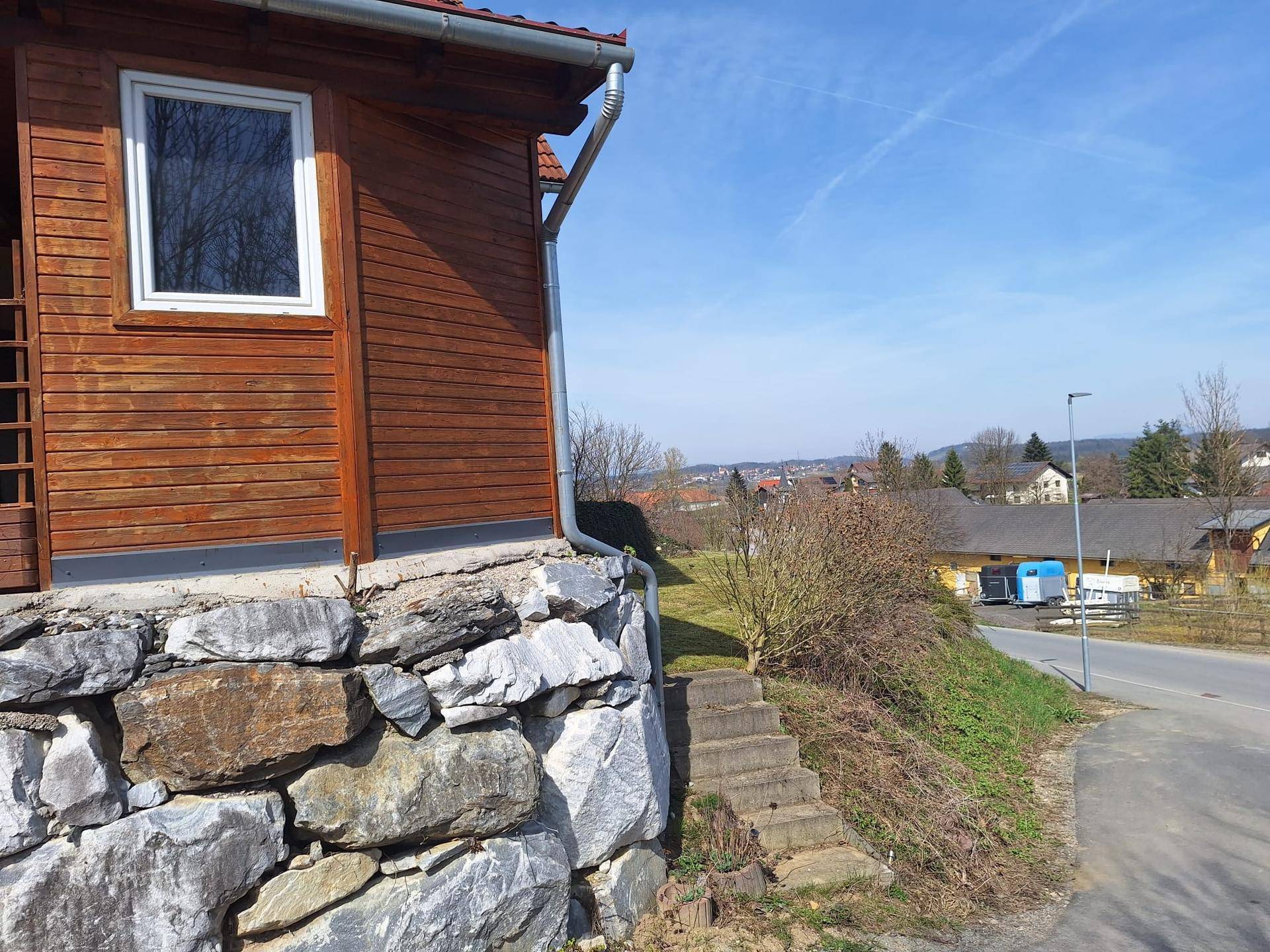 Detailansicht der Holzverkleidung des Anbaus und der Natursteinmauer am Hang.