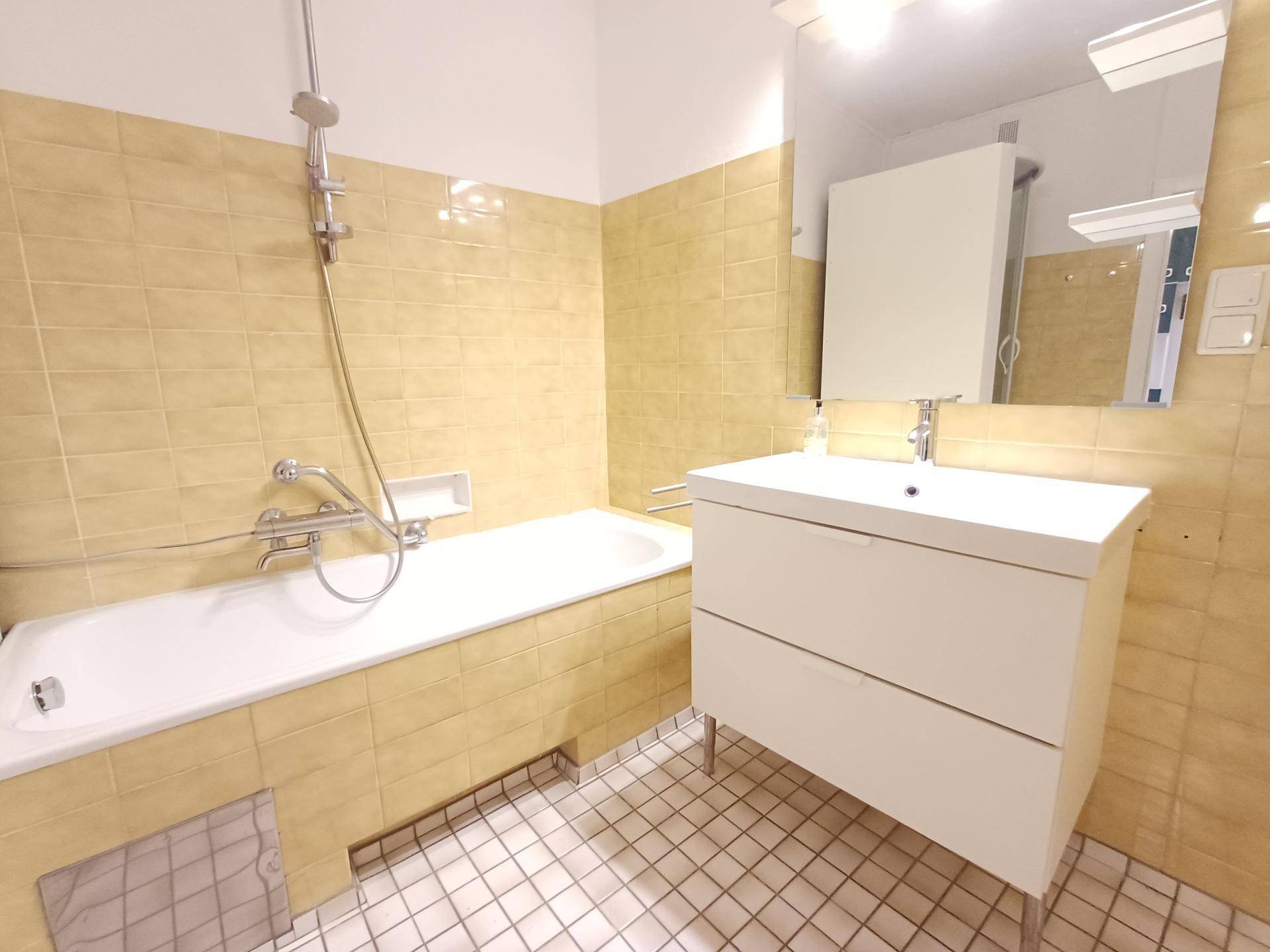 Badezimmer mit gelben Fliesen, Badewanne und modernem Waschtisch mit Spiegelschrank.