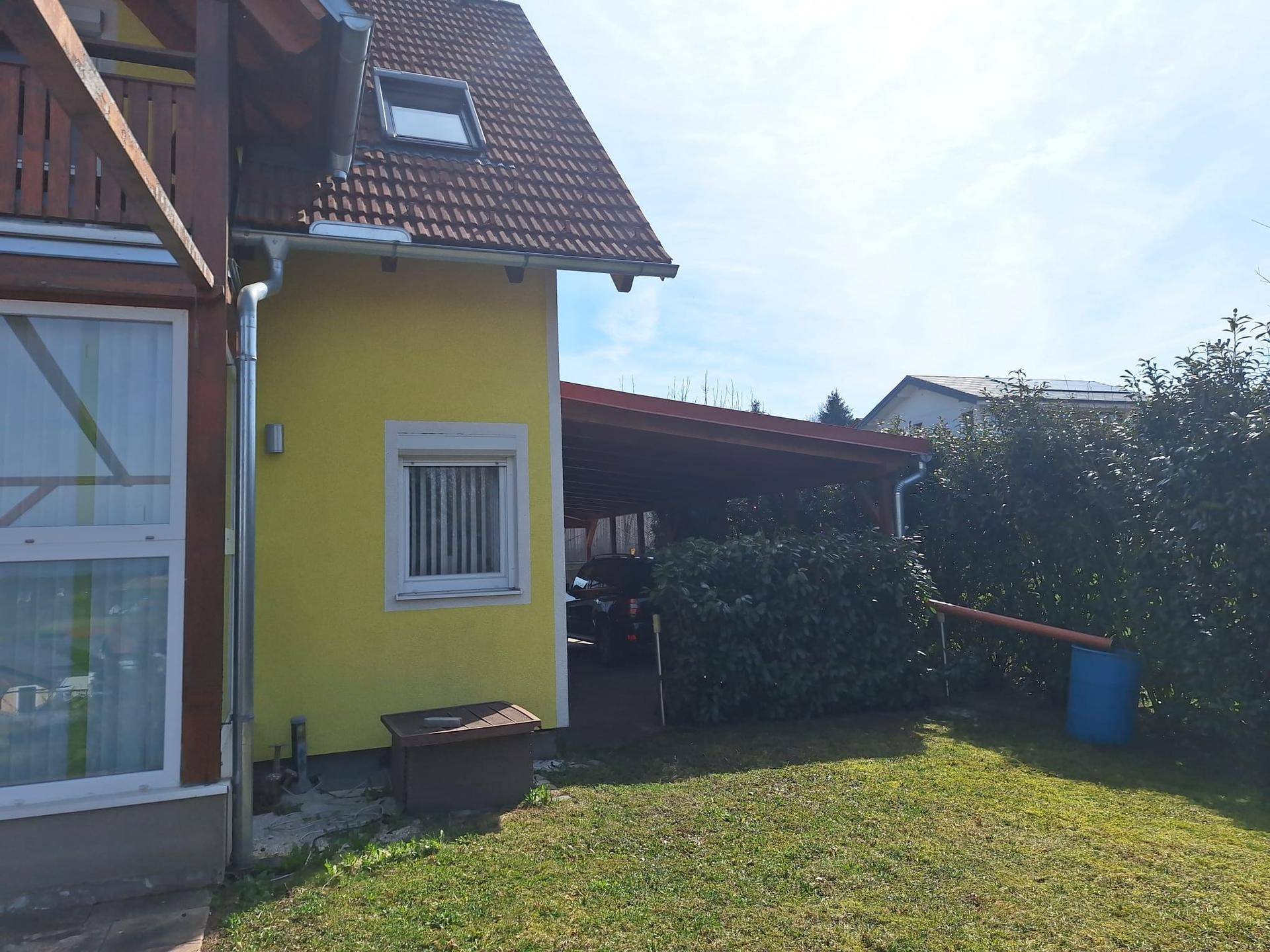 Seitenansicht des Hauses mit Carport und einem kleinen Gartenbereich mit Hecke.