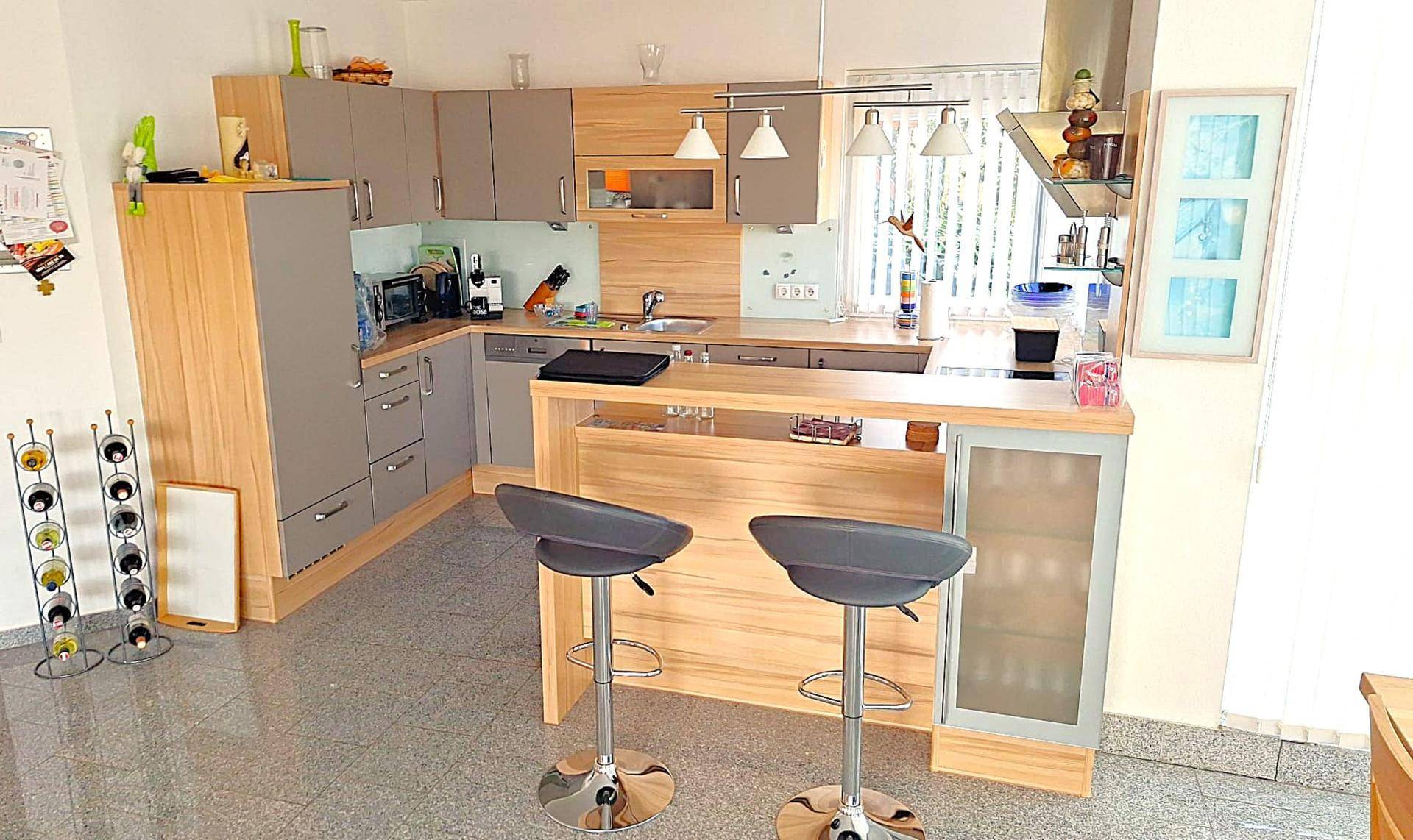 Moderne Einbauküche mit Holz- und Grautönen, Kücheninsel und Barhockern auf Fliesenboden.