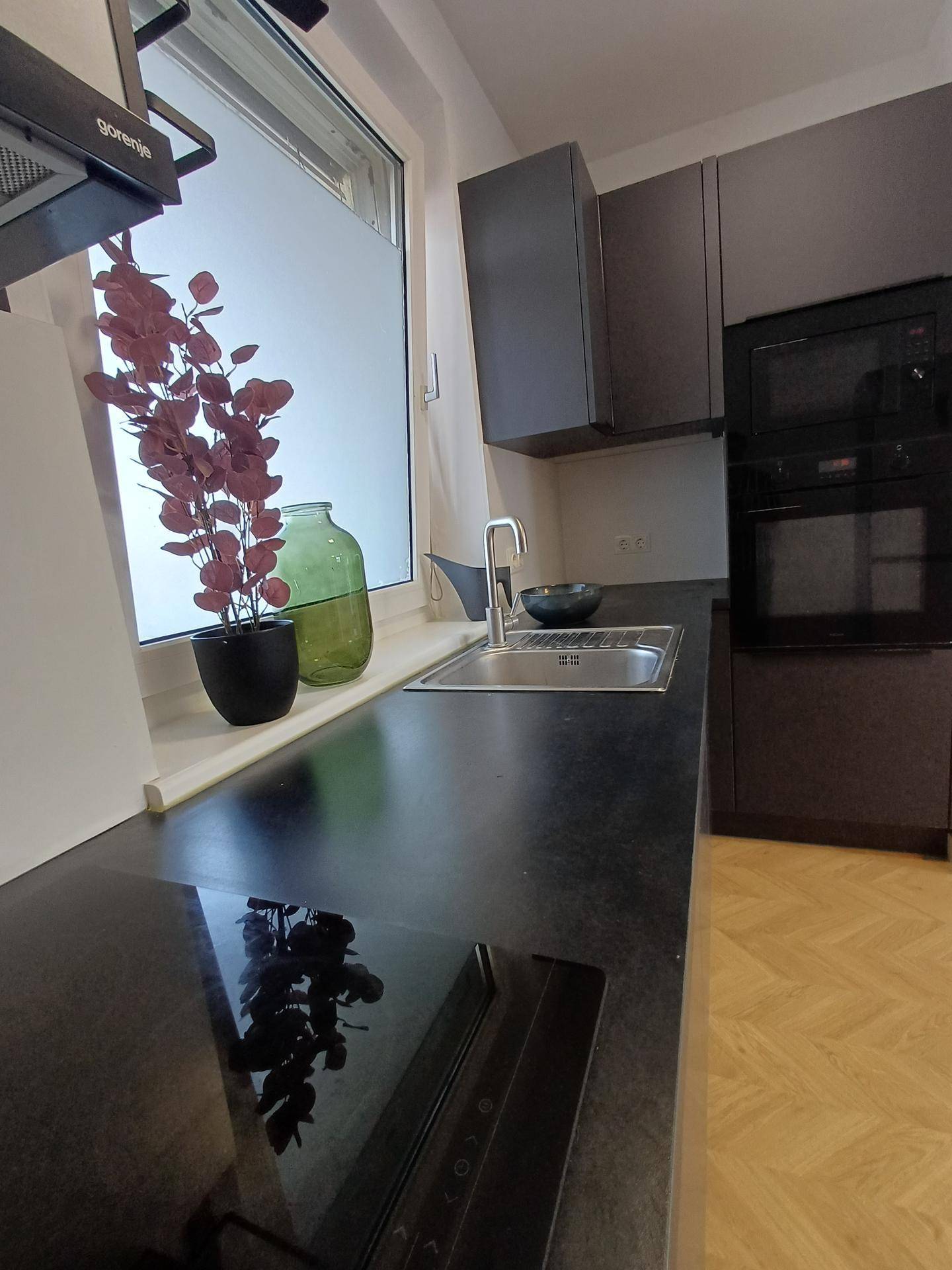 Moderne Küche mit dunklen Schränken, schwarzer Arbeitsplatte und Induktionskochfeld, mit Fenster.
