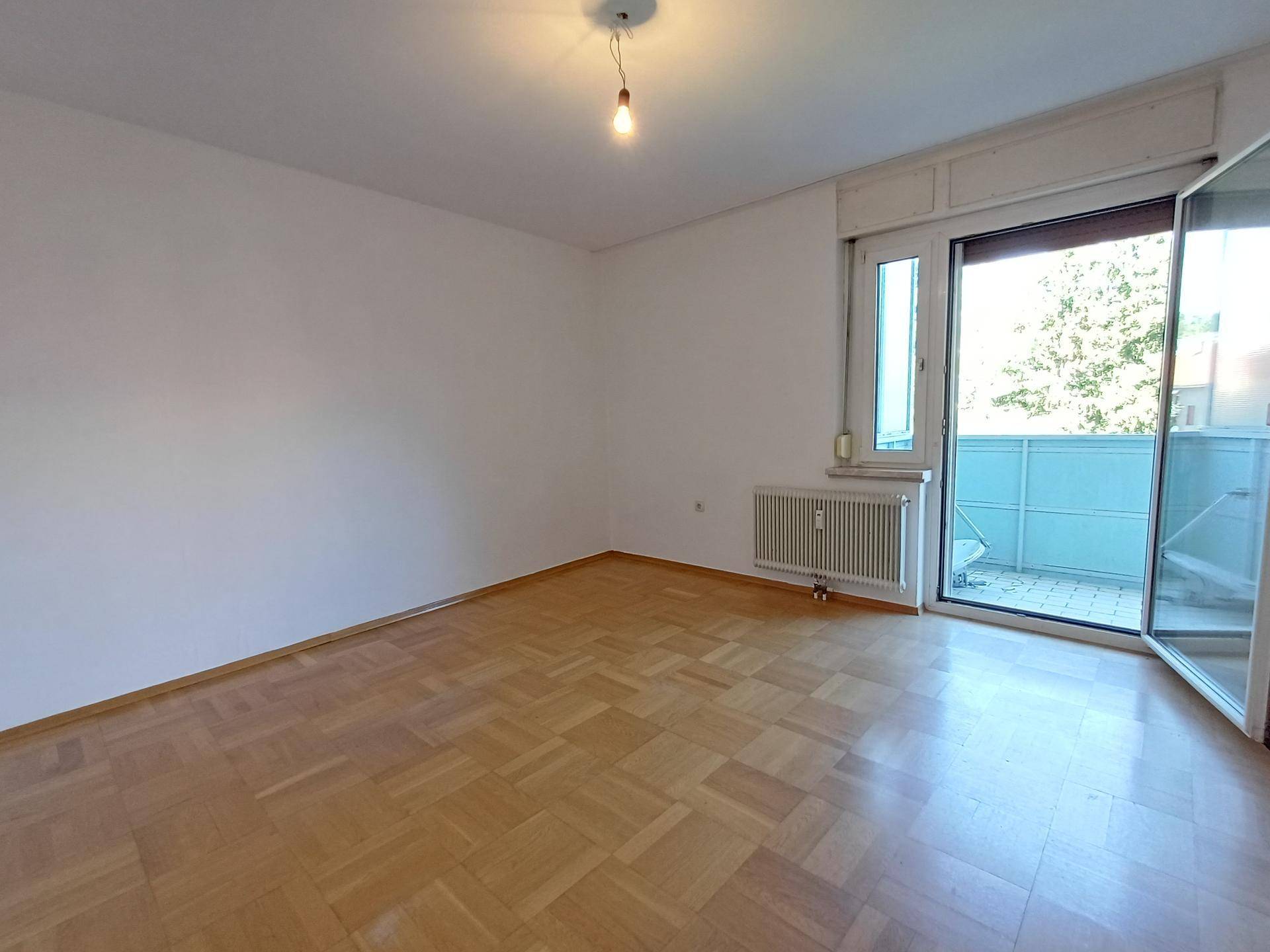 Helles Zimmer mit Parkettboden und direktem Zugang zu einem sonnigen Balkon.