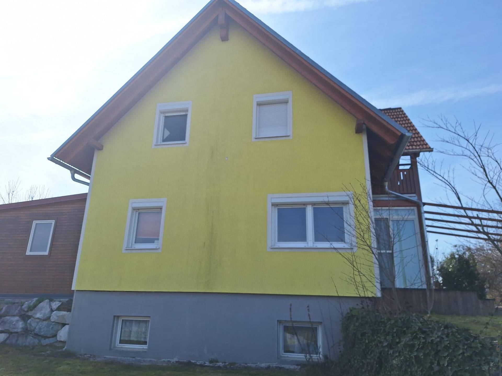 Seitenansicht des Hauses mit gelber Fassade, roten Dachziegeln und Fenstern.