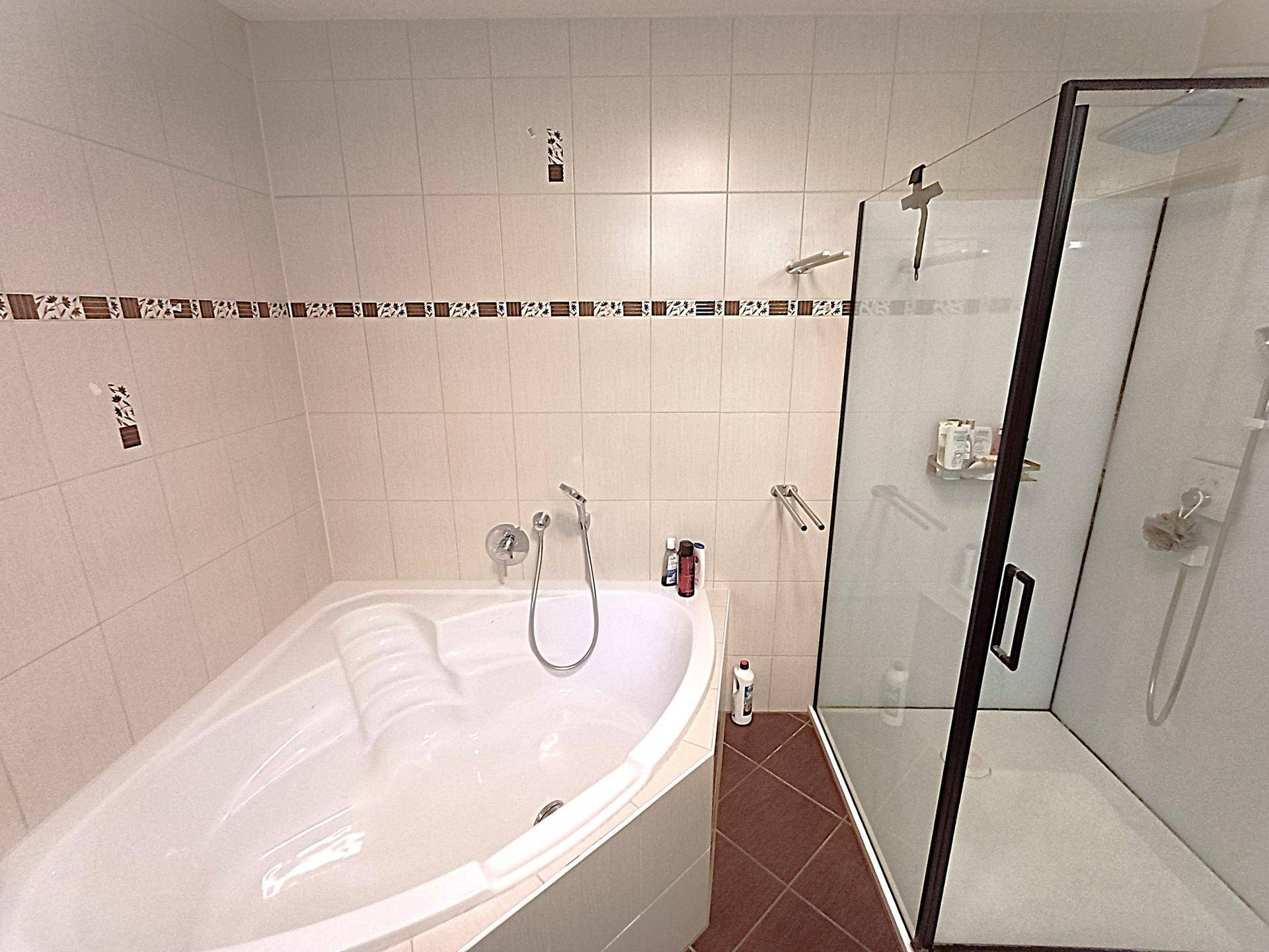Badezimmer mit Eckbadewanne, Duschkabine und hellen Fliesen.