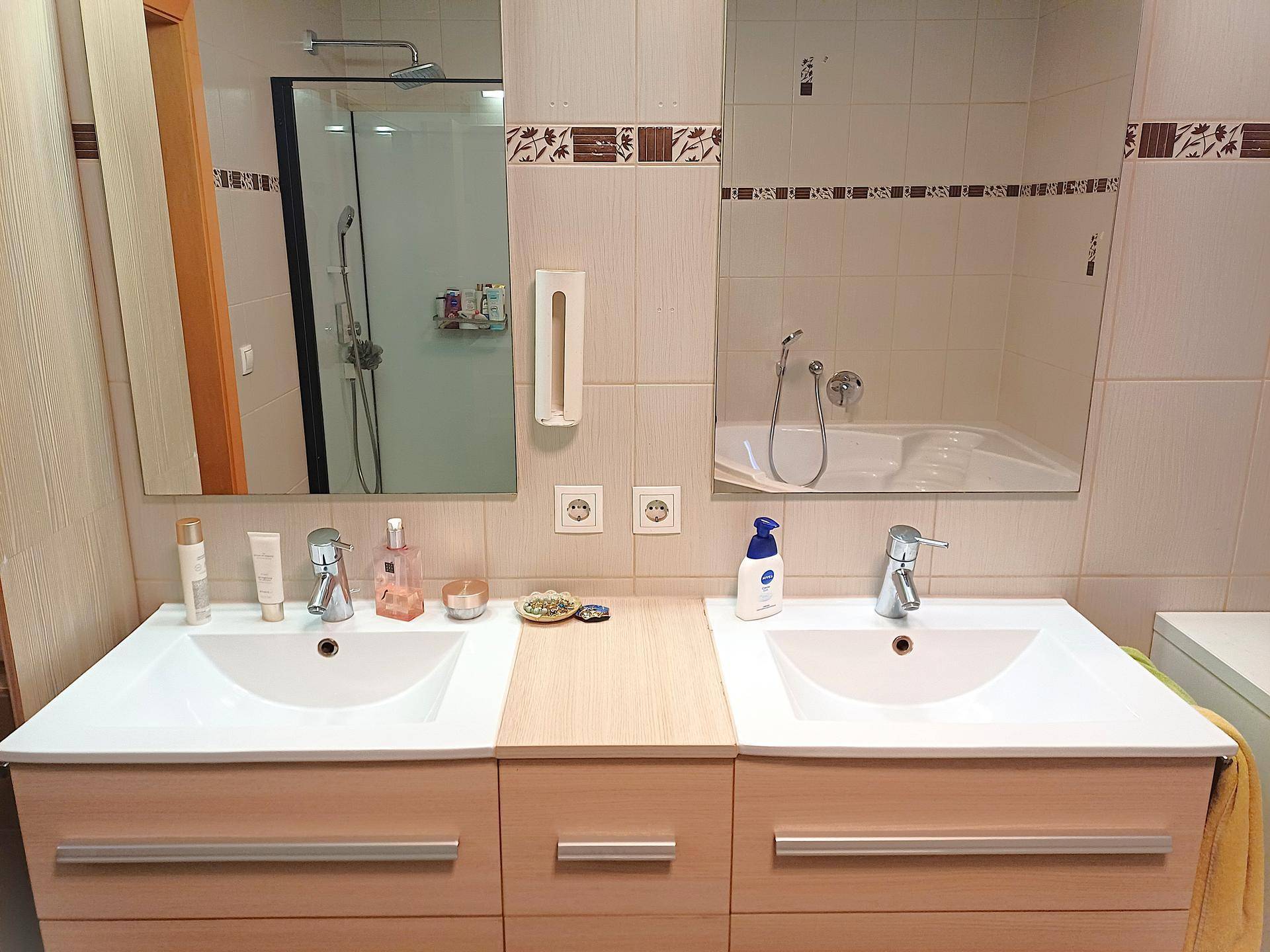 Badezimmer mit Doppelwaschbecken, großem Spiegel und hellen Fliesen.