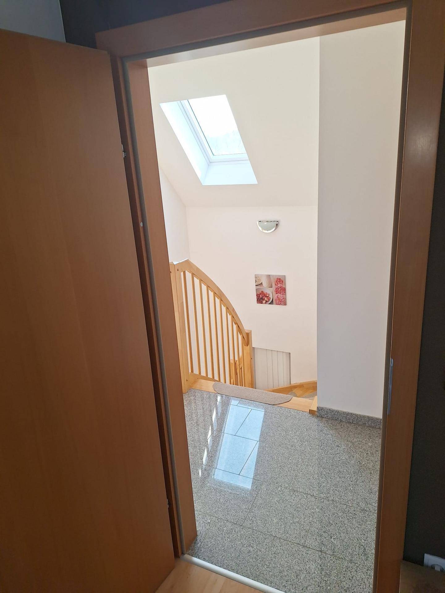 Heller Treppenaufgang mit Holzgeländer und Granitboden, führt in die oberen Etagen.
