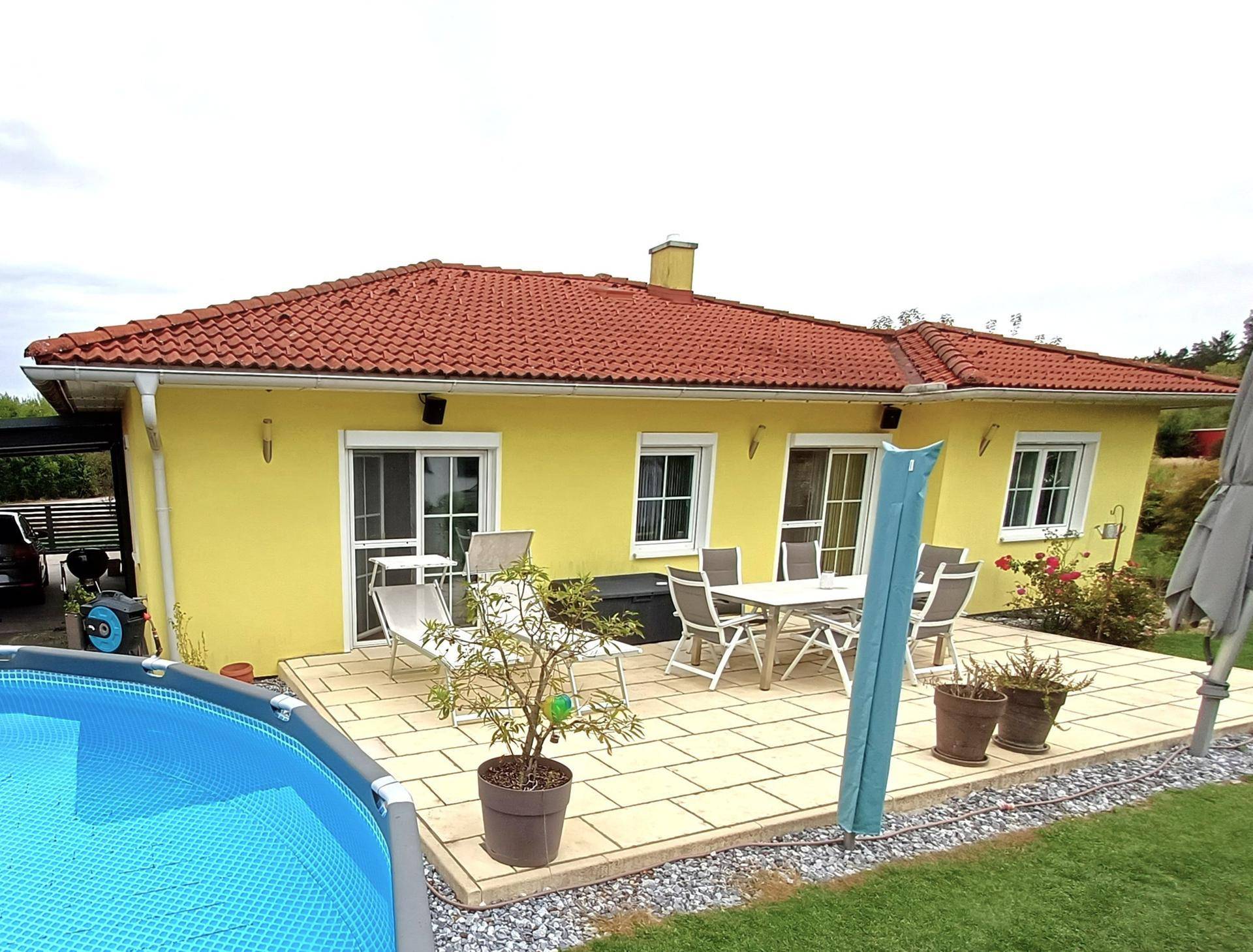 Terrasse mit Gartenmöbeln und einem aufgestellten Pool, umgeben von Rasenfläche.