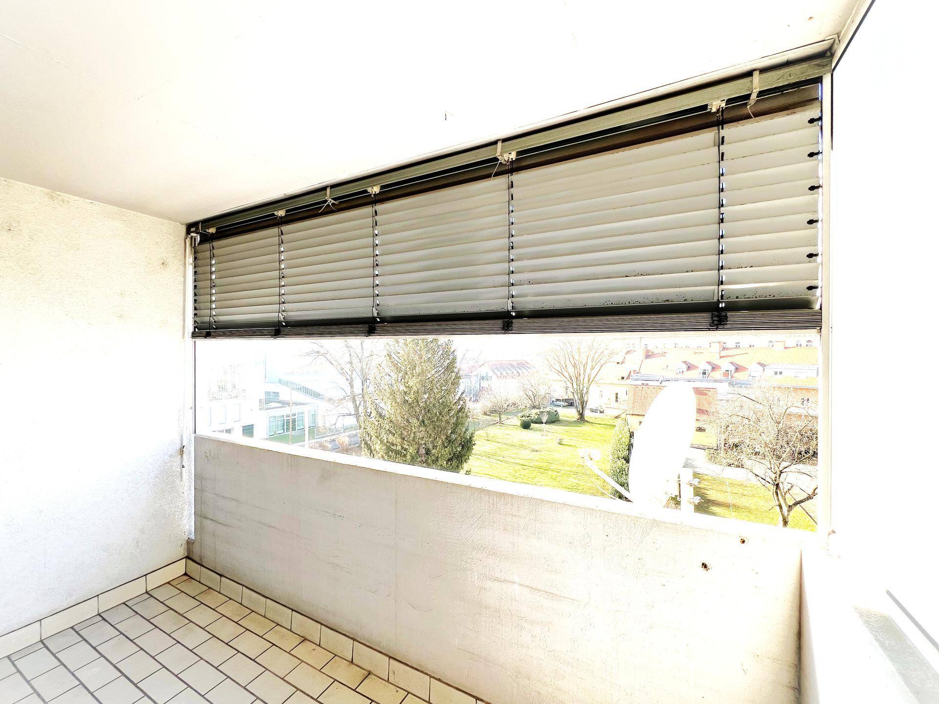 Heller Balkon mit Fliesenboden und Jalousien, bietet einen angenehmen Blick ins Grüne.