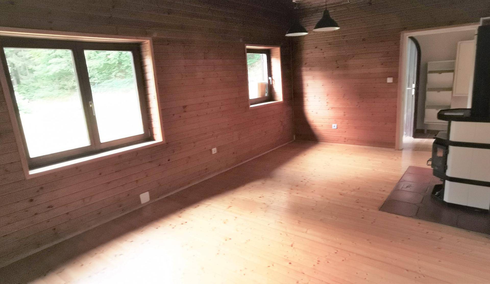Helles Wohnzimmer mit Holzwänden, Holzboden und einem traditionellen Kaminofen.
