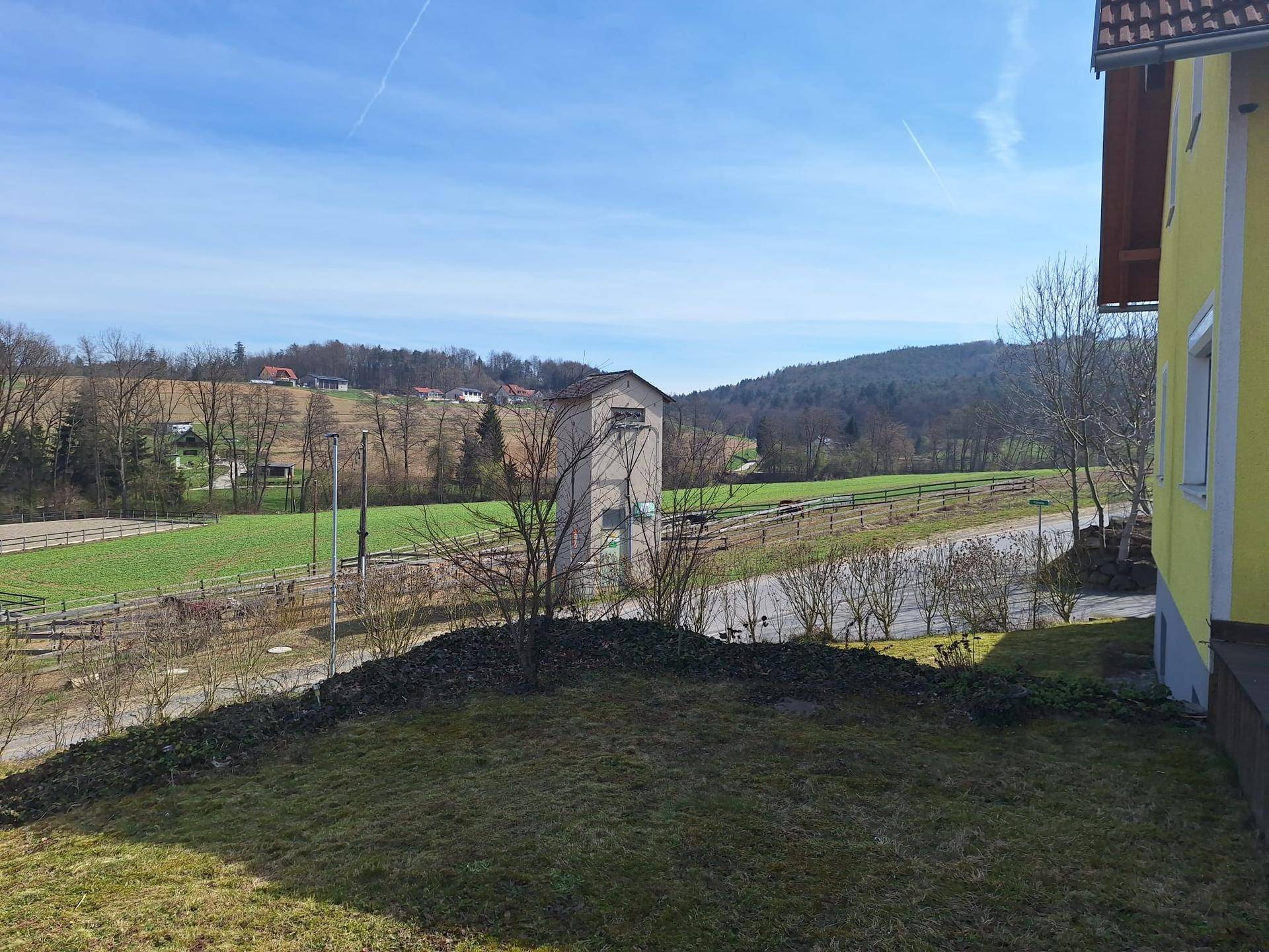 Weitläufiger Blick über grüne Felder und Hügel mit einem Reitplatz in der Ferne.