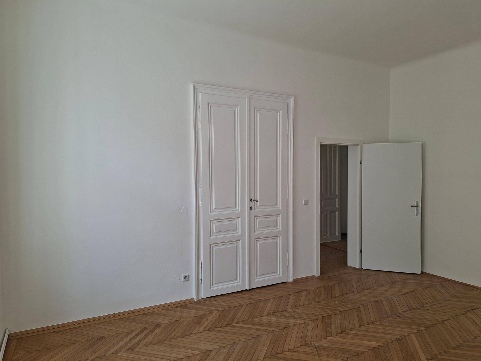 Helles Zimmer mit Fischgrätparkettboden und eleganten Doppeltüren, die den Raum öffnen.