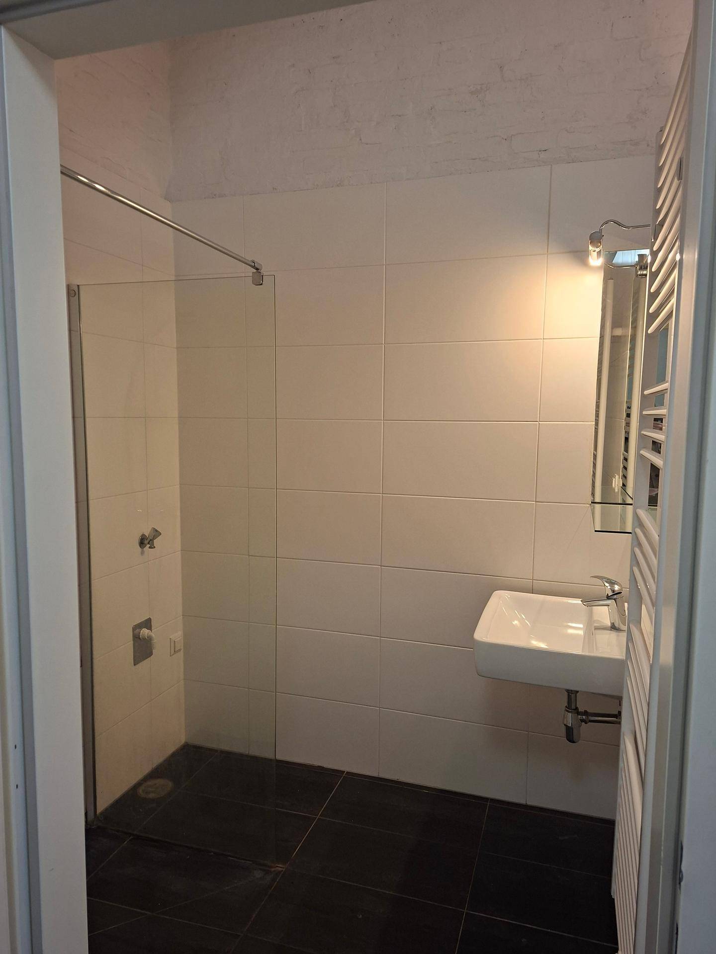Modernes Badezimmer mit Duschkabine, Waschbecken und weißen Fliesen an den Wänden.